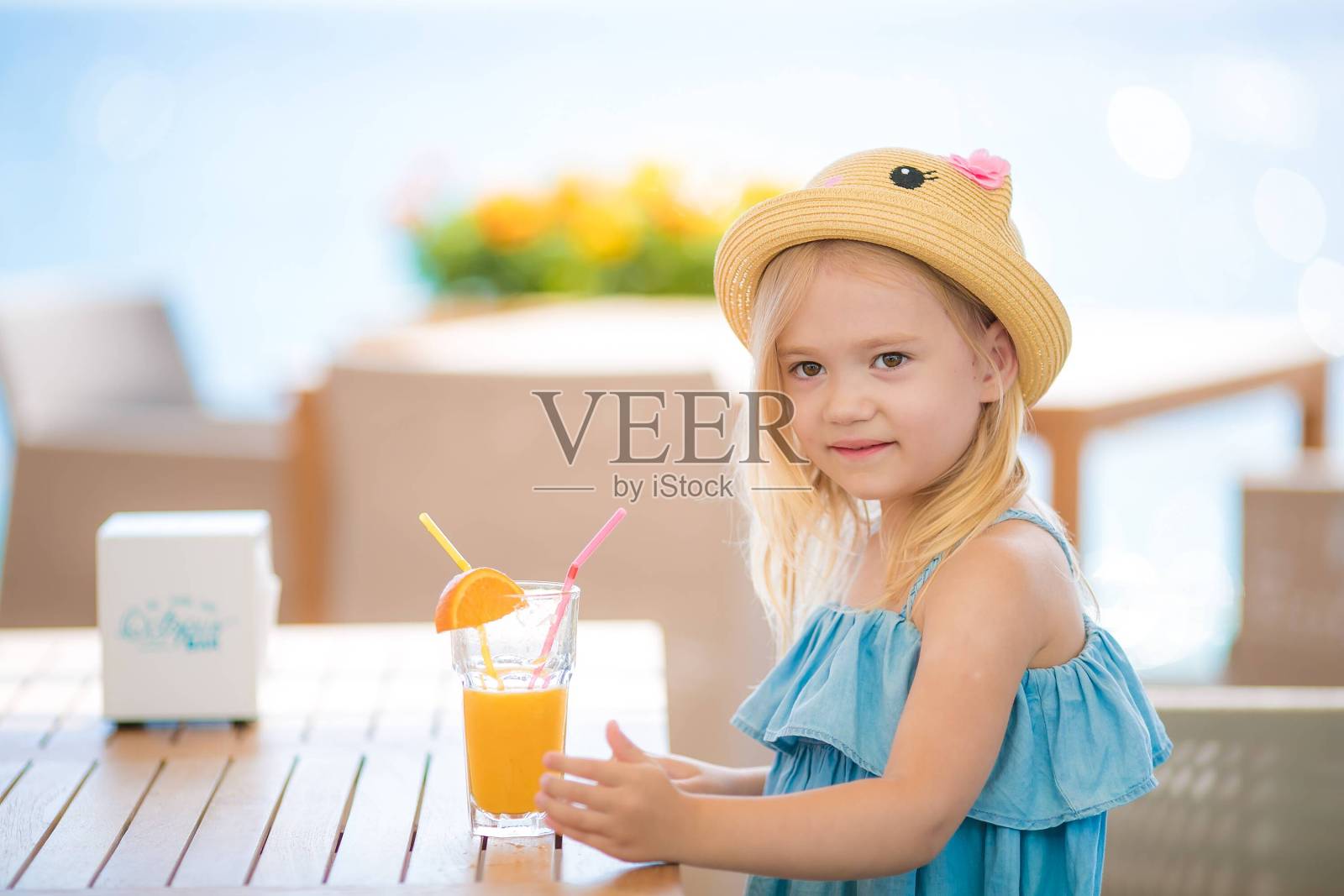 漂亮的金发女孩坐在户外咖啡馆的桌子边喝着果汁，吃着甜点照片摄影图片