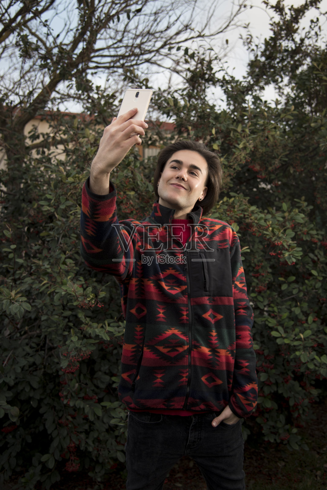 一个年轻人在一丛红色浆果前用手机拍照照片摄影图片