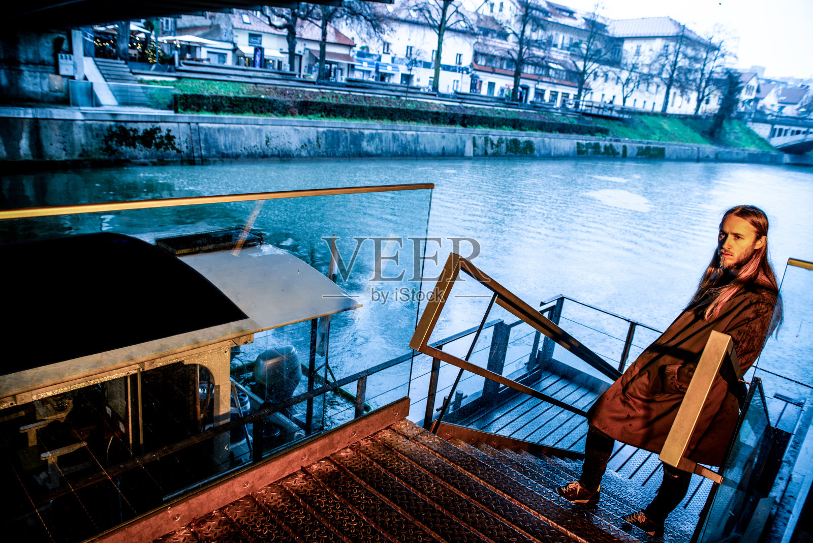 一个忧郁的成年男子倚靠在桥下的楼梯栏杆上，在一个寒冷的日子-库存照片照片摄影图片