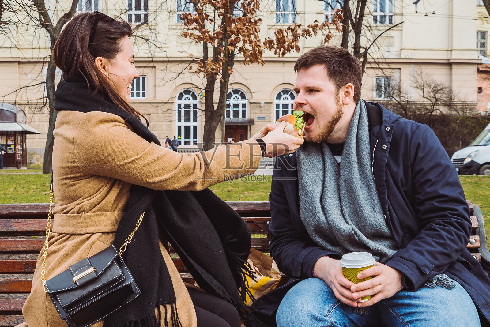 一对年轻的成年夫妇在城市公园的长椅上吃快餐照片摄影图片