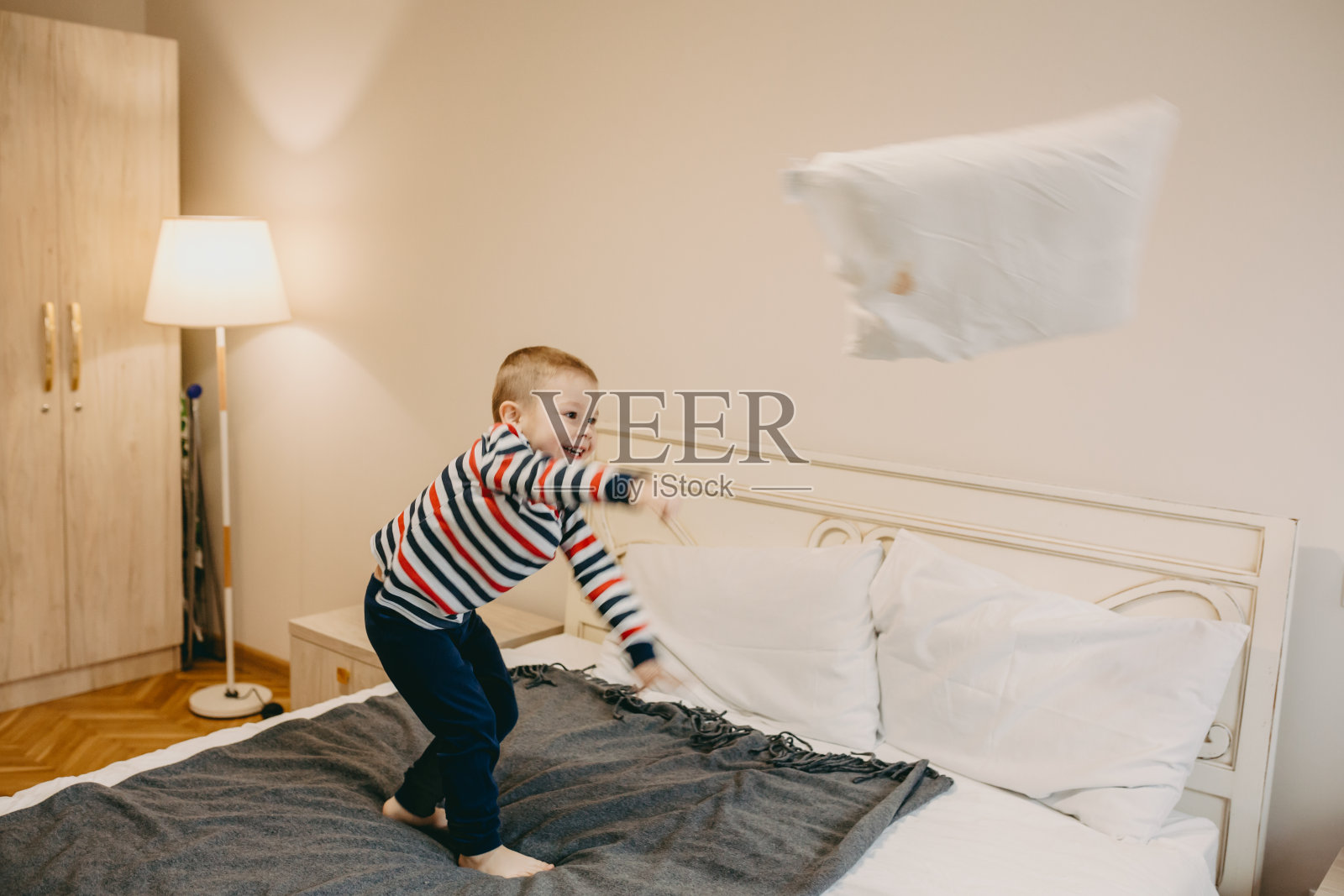 可爱的白人小男孩站在床上扔掉一个枕头照片摄影图片