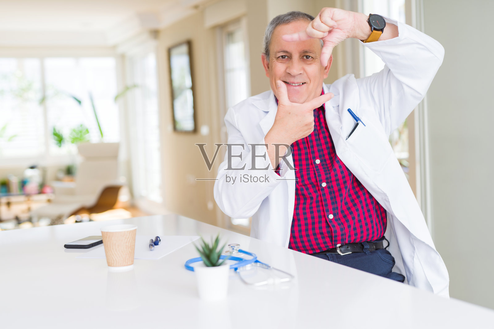 英俊的资深医生男人穿着医疗外套在诊所微笑做框架与手和手指与幸福的脸。创意和摄影概念。照片摄影图片