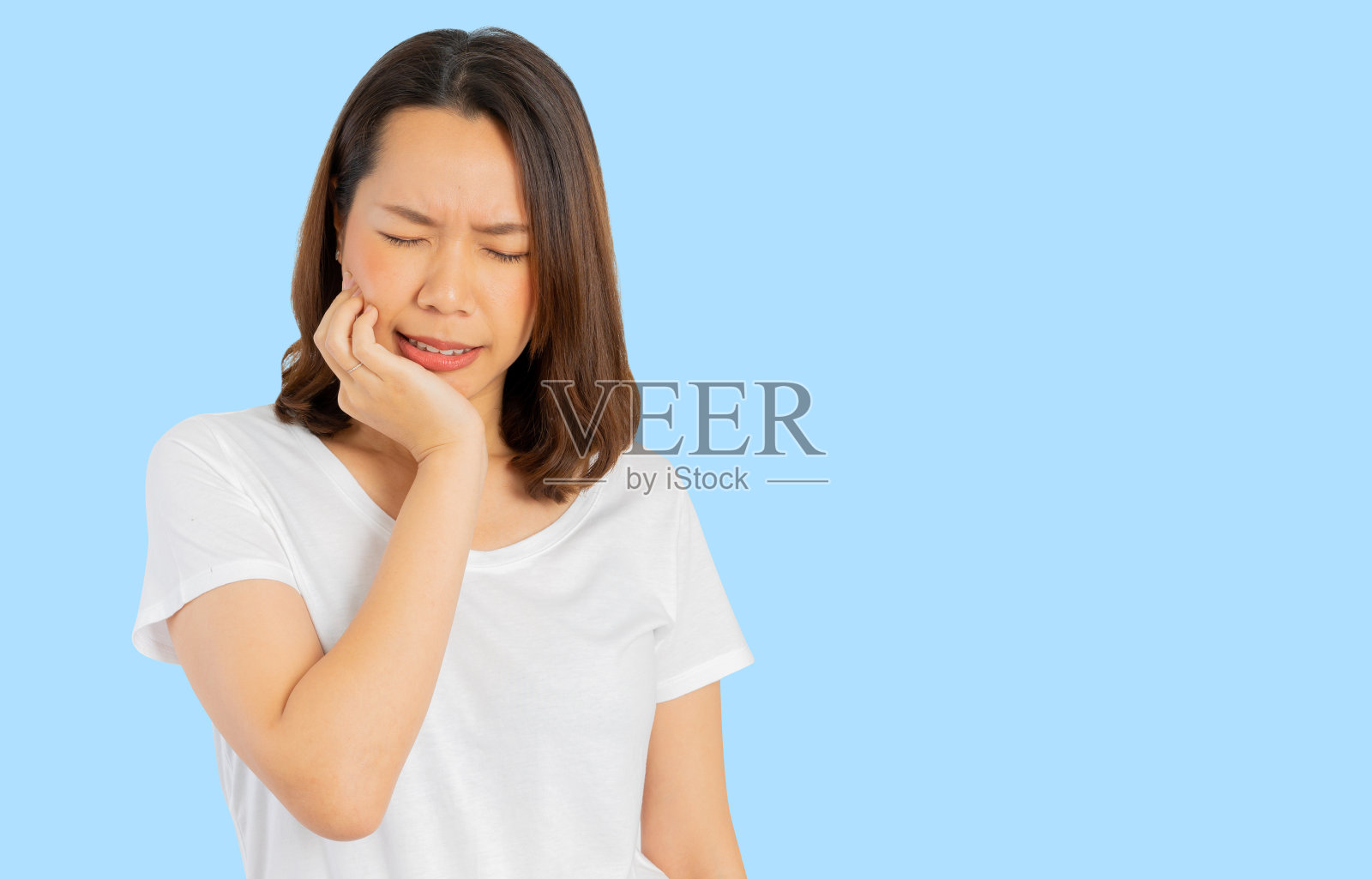 闭合成年亚洲妇女用手按摩面颊引起的牙痛(智齿)孤立在蓝色背景的牙科保健概念照片摄影图片