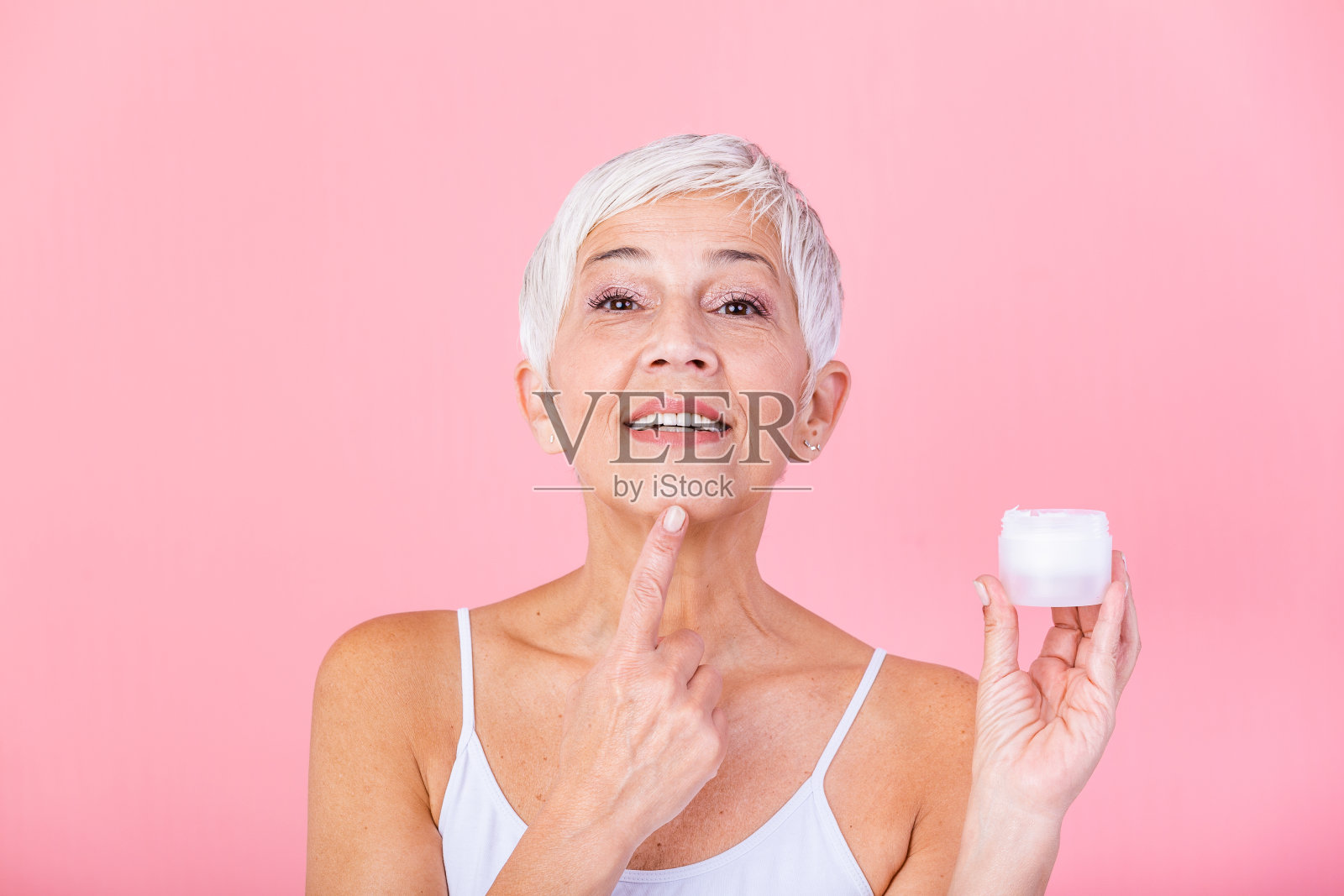 微笑的老年妇女应用抗衰老乳液去除皱纹。成熟的女人用化妆品来掩盖皱纹。女士使用日间保湿霜来对抗皮肤的老化。照片摄影图片