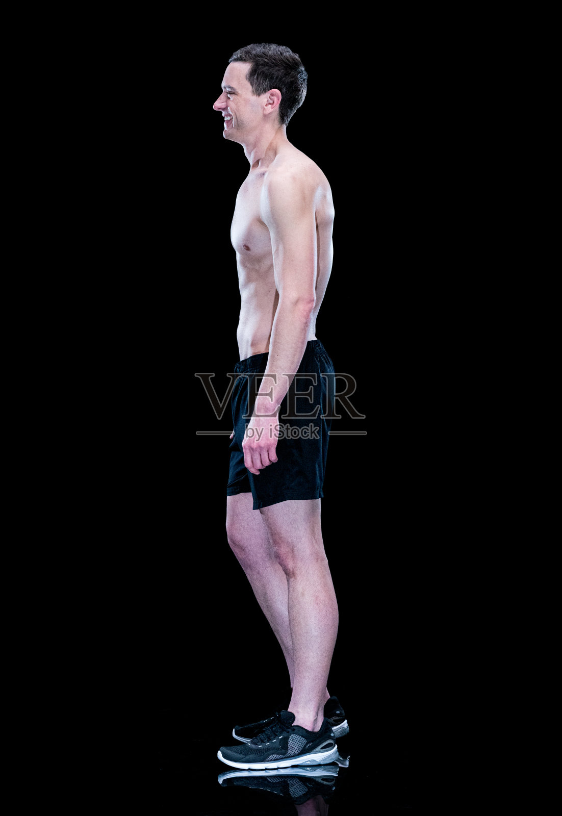 白人年轻男性运动员穿着短裤在黑色背景前运动照片摄影图片