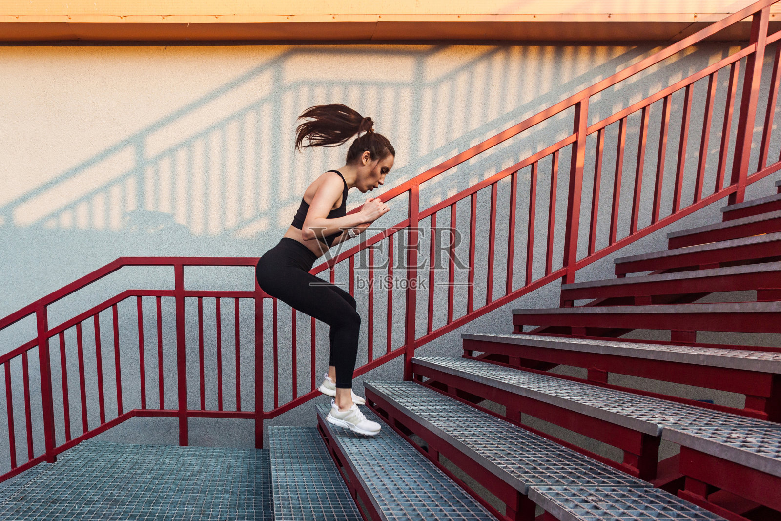 健美运动员美女穿着紧身运动服在楼梯上跳跃，慢跑前热身，在楼梯上训练照片摄影图片