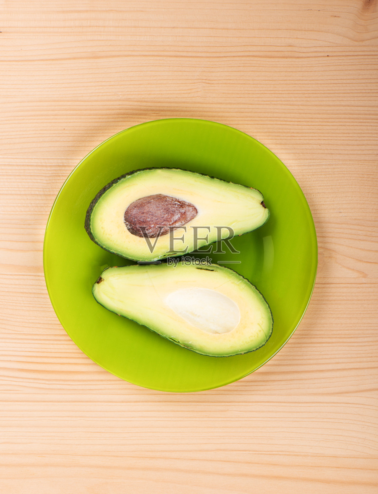 把成熟的牛油果切成片放在绿色的盘子上，放在木制的背景上。照片摄影图片