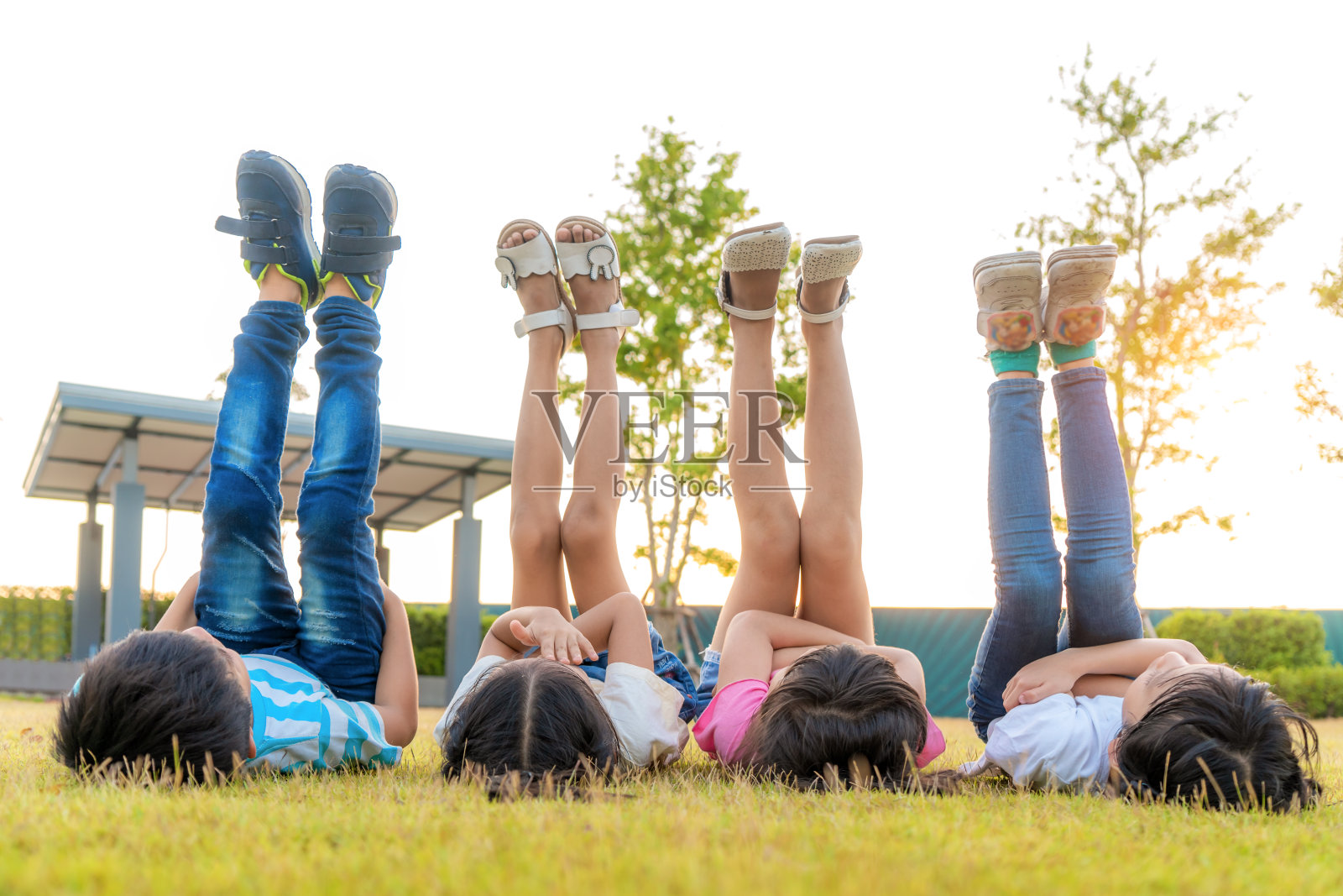 在阳光明媚的夏日里，一群快乐的亚洲幼儿园小朋友朋友们躺在草地上，一起把腿抬向天空。照片摄影图片