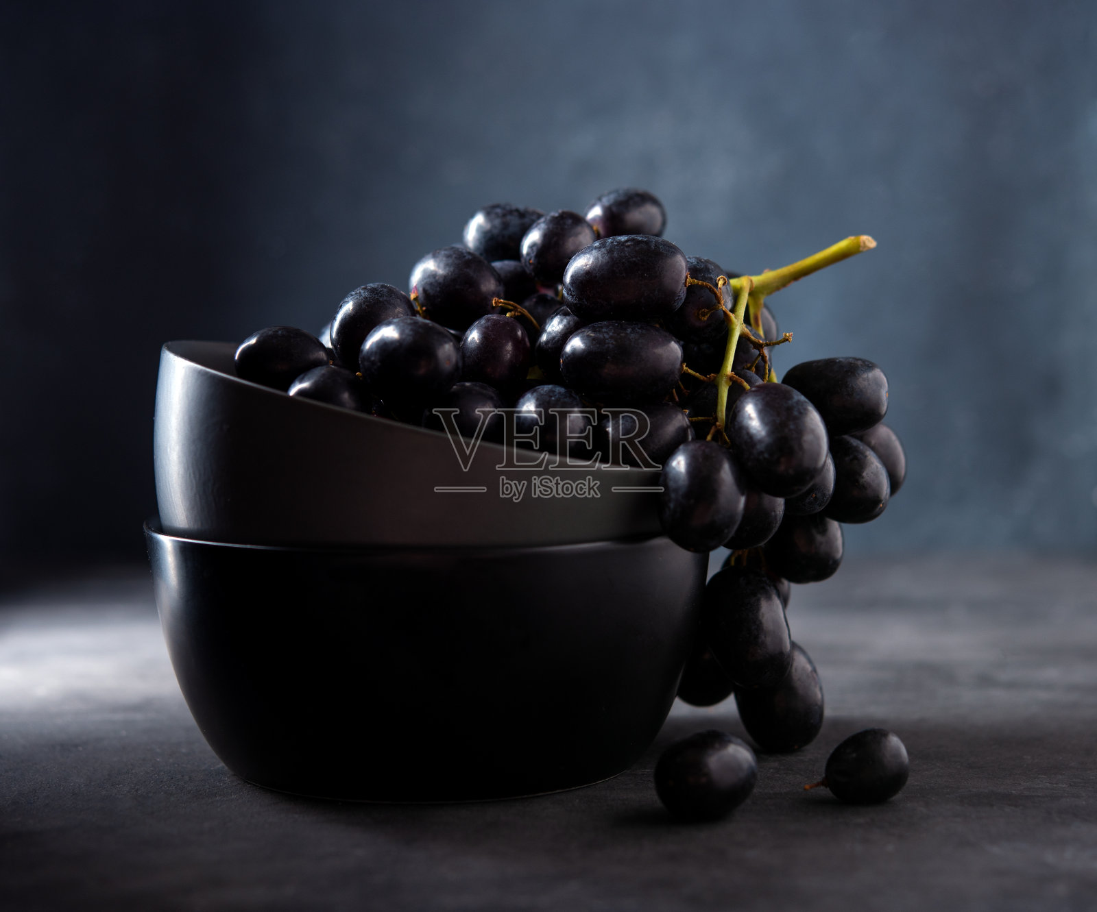 深灰色的桌子上，深灰色的碗里放着一串多汁的黑葡萄照片摄影图片
