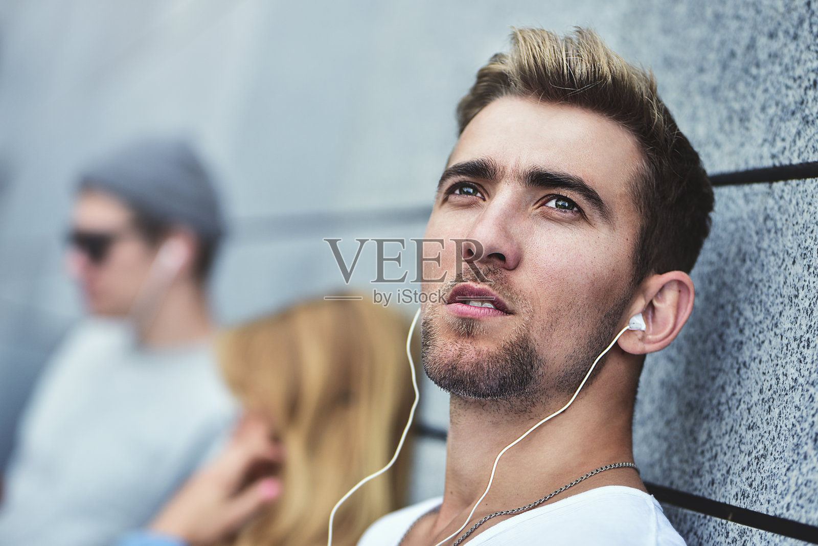 年轻迷人的青少年戴着同样的耳机听音乐，穿着时髦的衣服，背景是灰色的墙。照片摄影图片