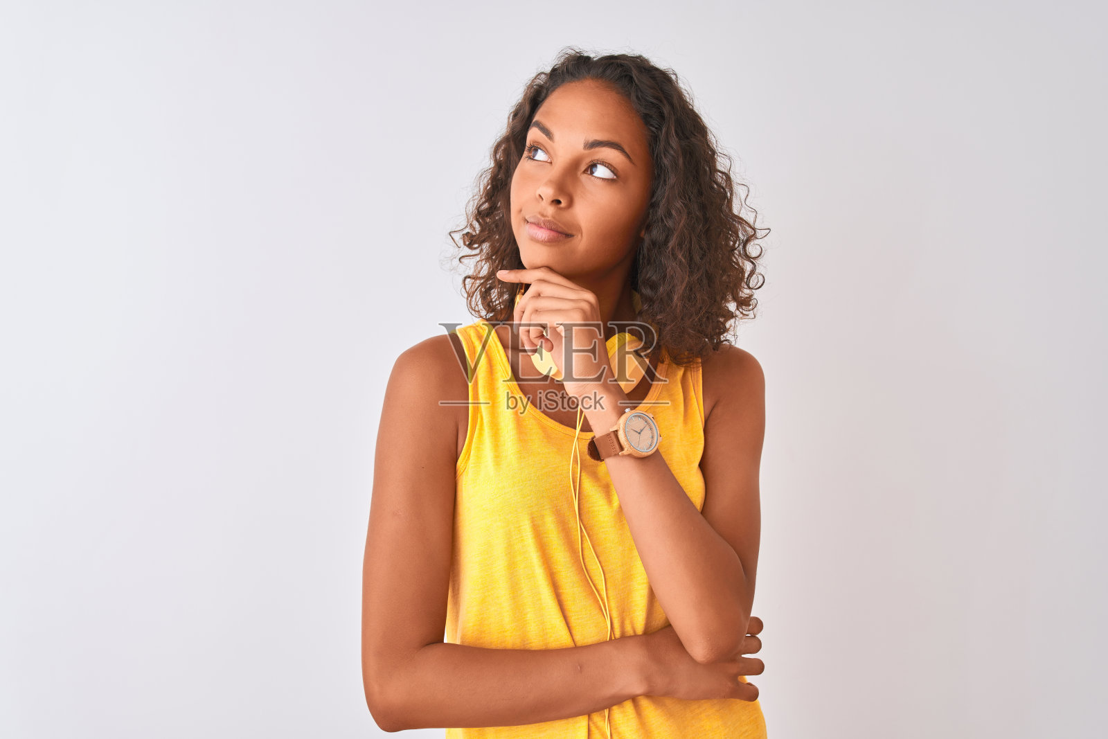年轻的巴西女子戴着黄色耳机在孤立的白色背景下，手放在下巴思考问题，沉思的表情。带着沉思的微笑。怀疑的概念。照片摄影图片
