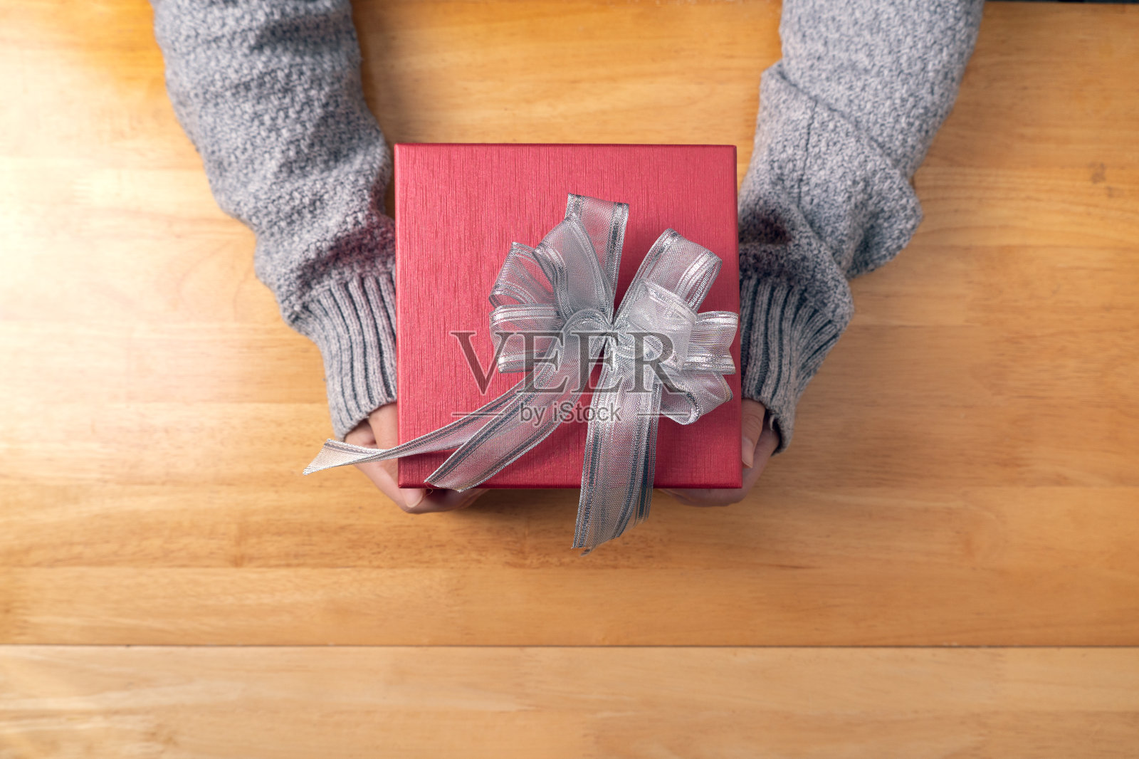 女人穿着毛衣，手握红色的礼物盒在木头桌子上，礼物为圣诞节，新年，情人节，生日和周年照片摄影图片