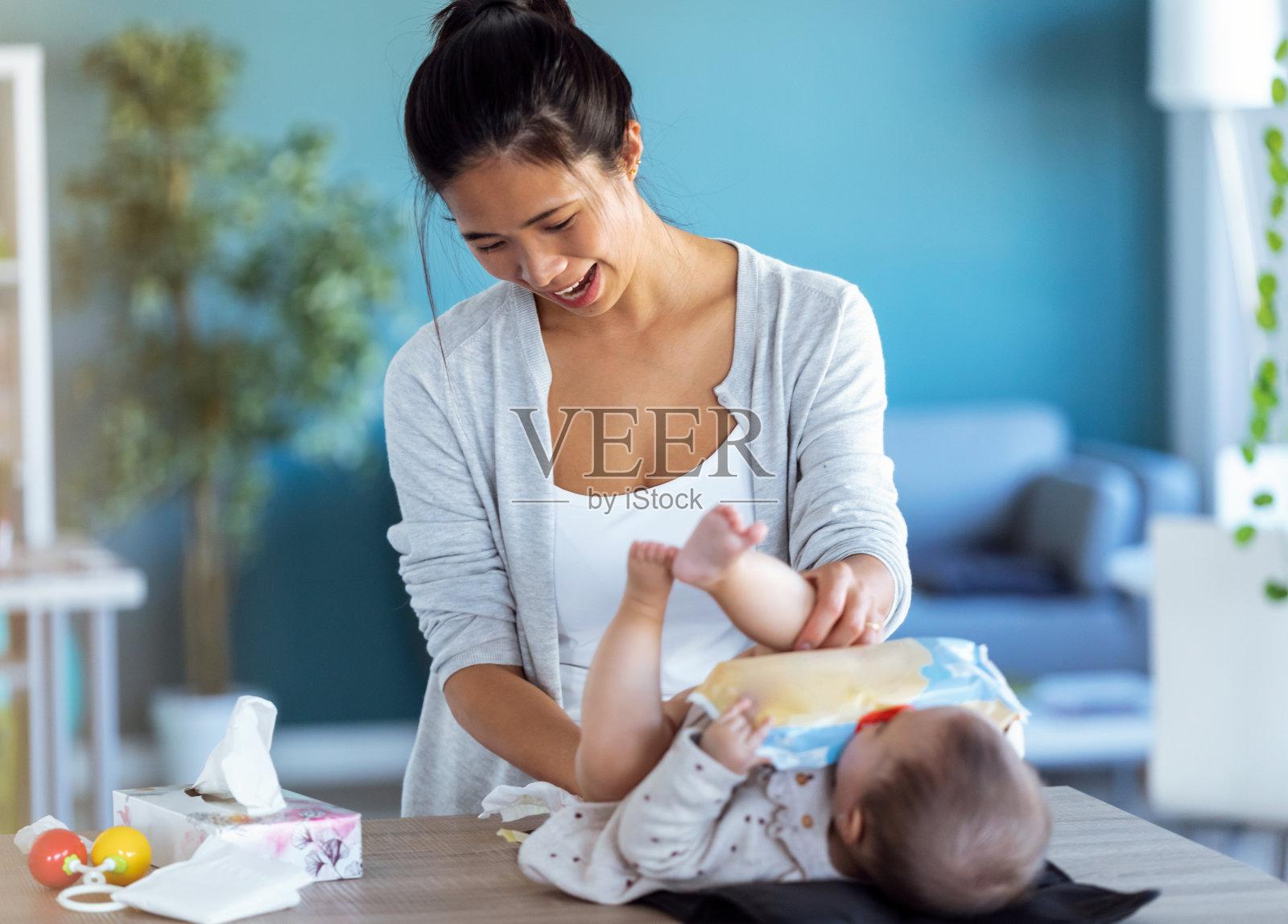 微笑的年轻妈妈在家里给宝宝换尿布的时候和他玩得很开心。照片摄影图片