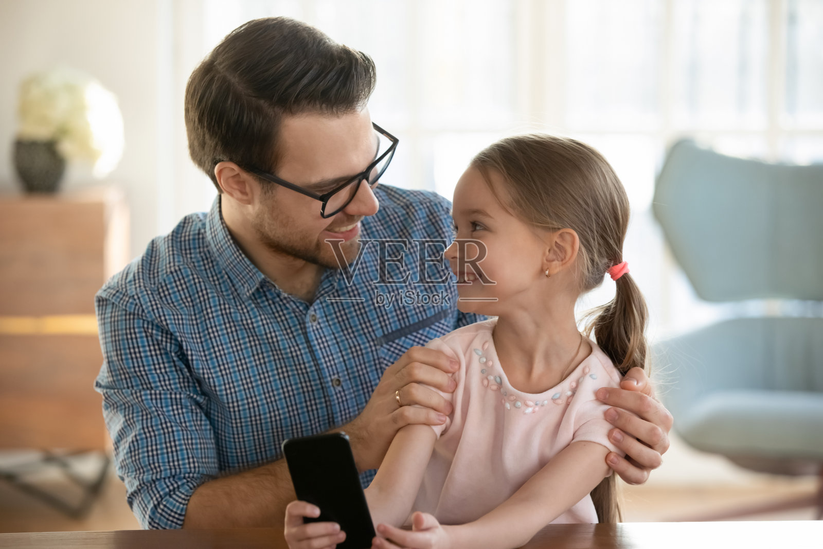年轻的爸爸用智能手机看着快乐的小女儿。照片摄影图片