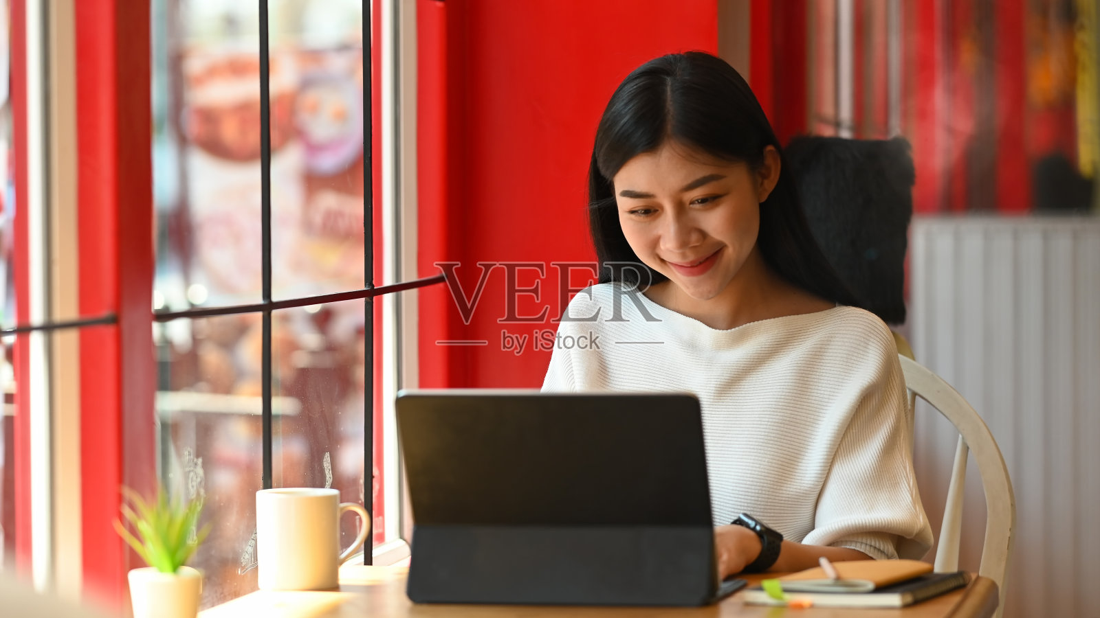 年轻美丽的女人在白色棉质衬衫作为会计工作微笑和工作/坐在现代工作桌子与舒适的客厅作为背景。照片摄影图片