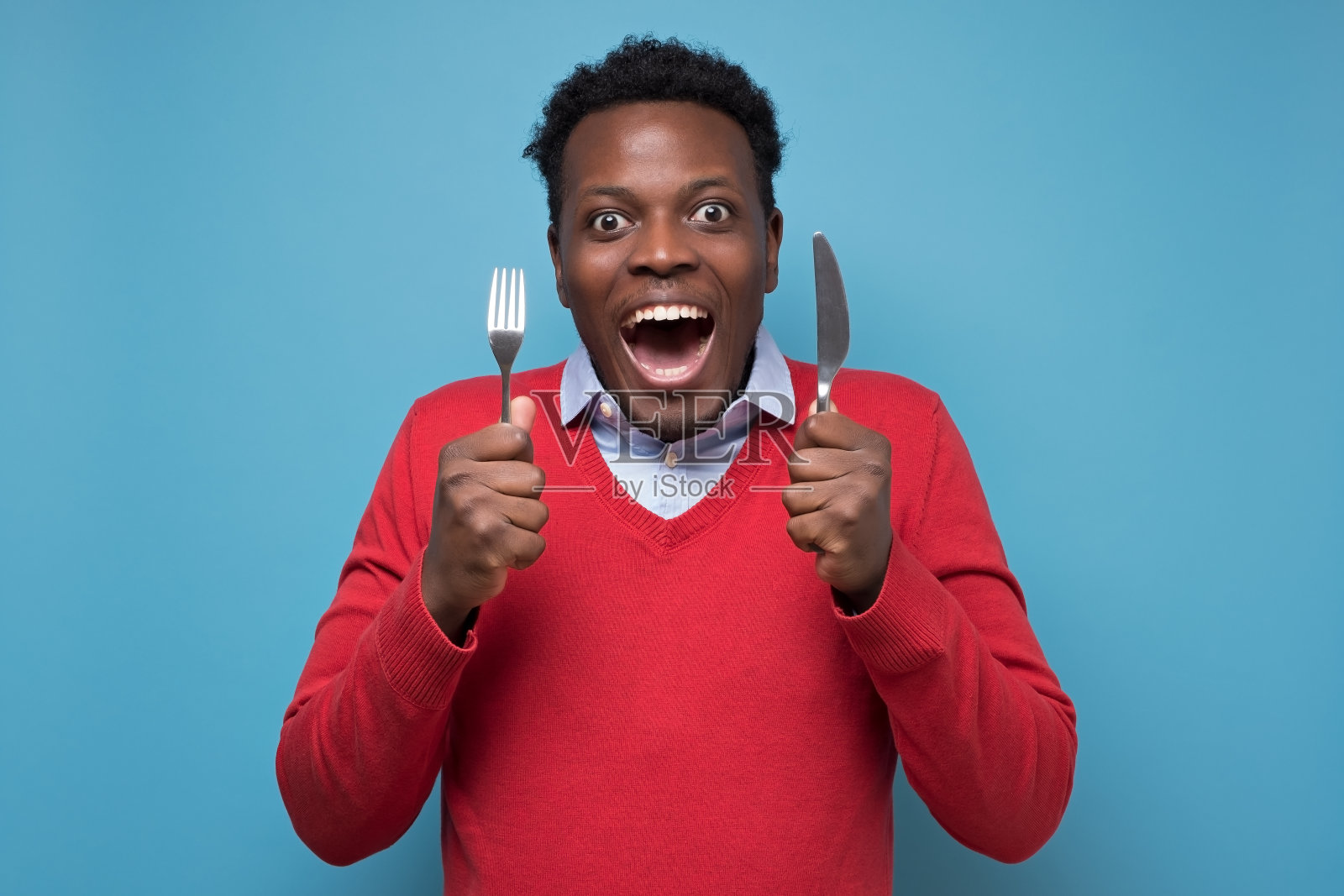 年轻饥饿的非洲男子拿着刀叉等待美味的饭菜。照片摄影图片