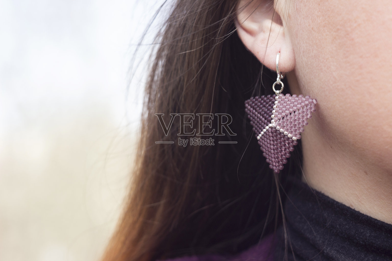耳朵上戴着珠子耳环的年轻女子。紫色耳饰，背景照片摄影图片