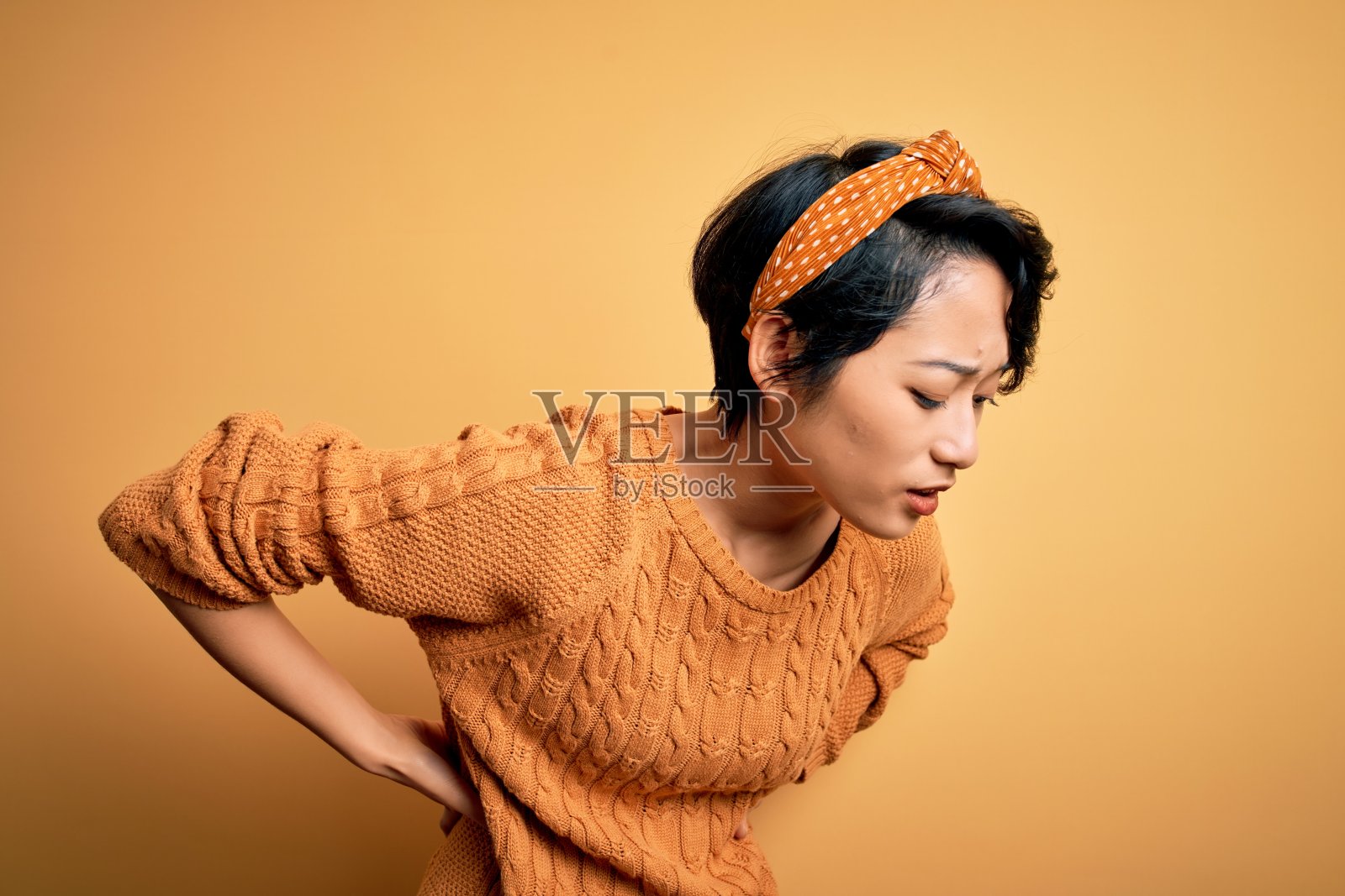 年轻美丽的亚洲女孩穿着休闲毛衣和冠冕站在黄色的背景照片摄影图片