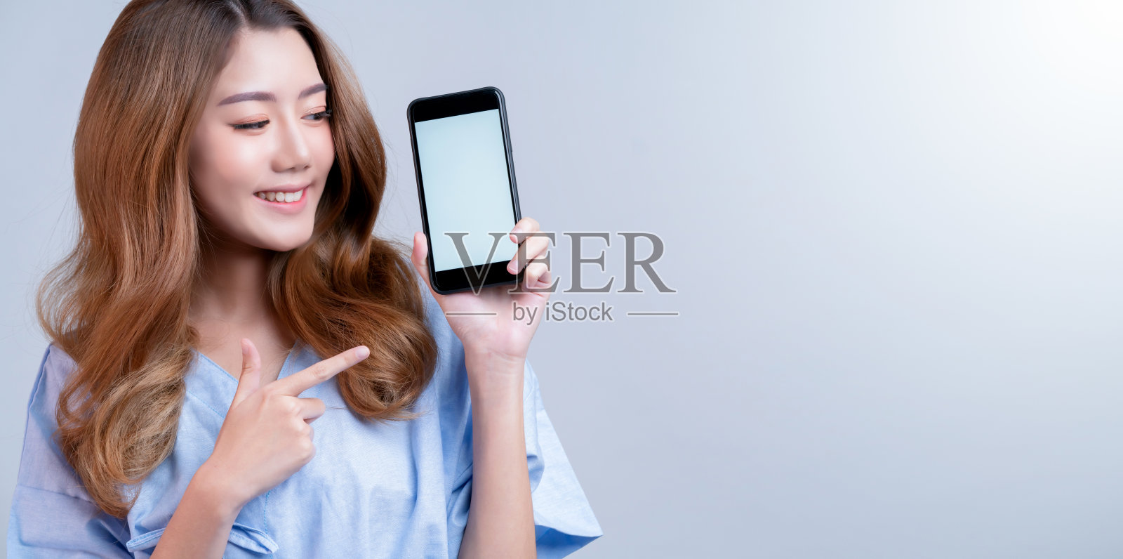 商业健康保险美丽的亚洲女性在医院制服微笑与手展示智能手机的快乐保险包装和推广与医院模糊的背景照片摄影图片