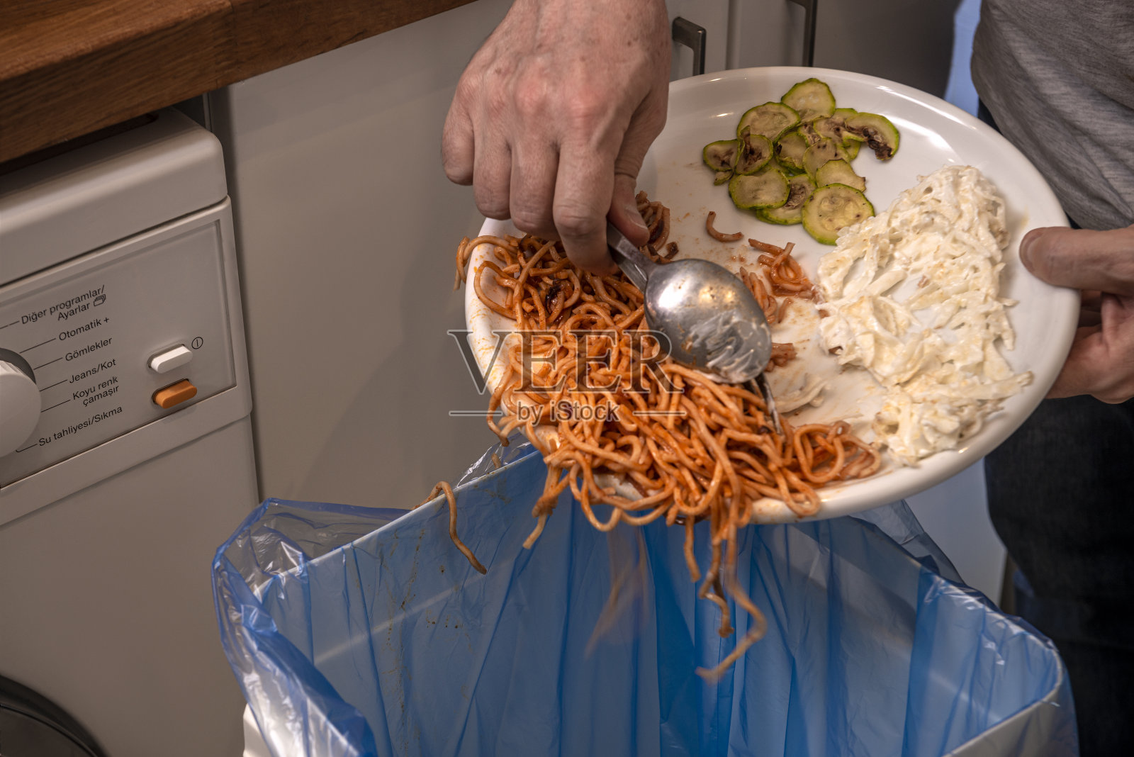 把吃剩的意大利面倒进垃圾桶。照片摄影图片