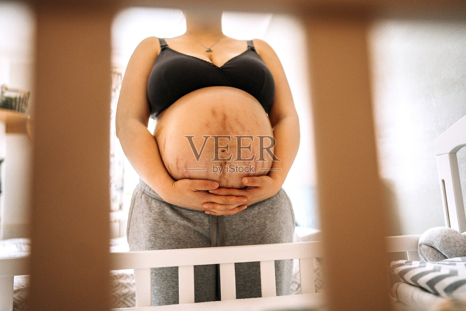 有妊娠纹的孕妇站在婴儿床旁照片摄影图片