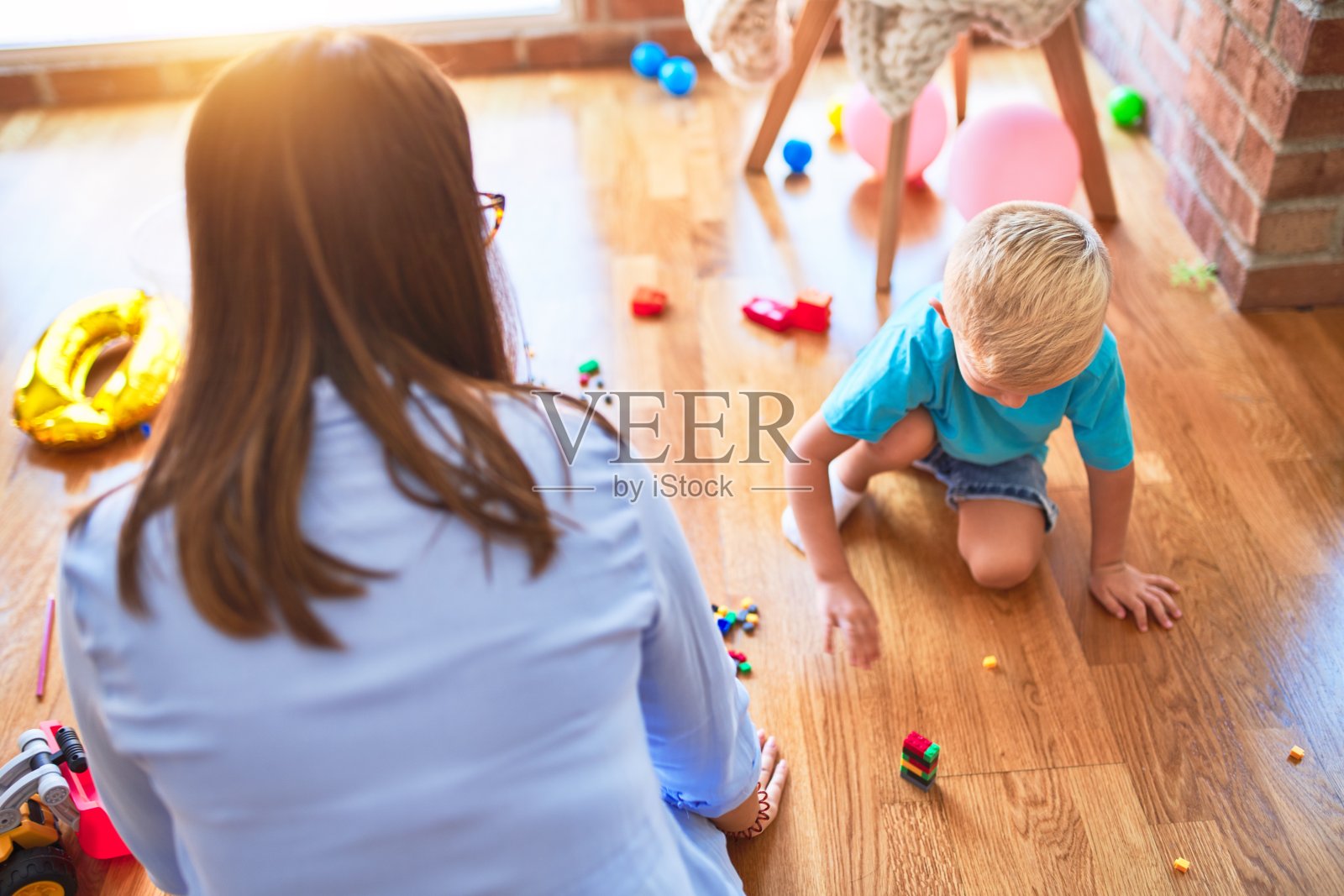 年轻的白人孩子在游戏学校和老师玩。妈妈和儿子在游戏室用玩具积木搭一座塔照片摄影图片