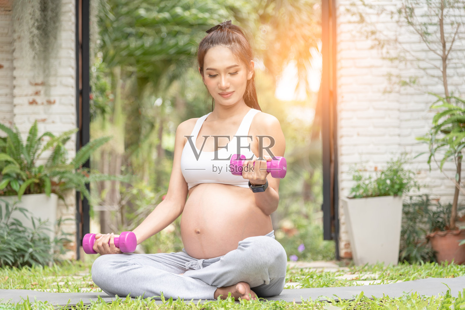 美丽的亚洲孕妇放松锻炼使用哑铃在公园。给宝宝的正确选择。在大自然中冥想的孕妇。照片摄影图片