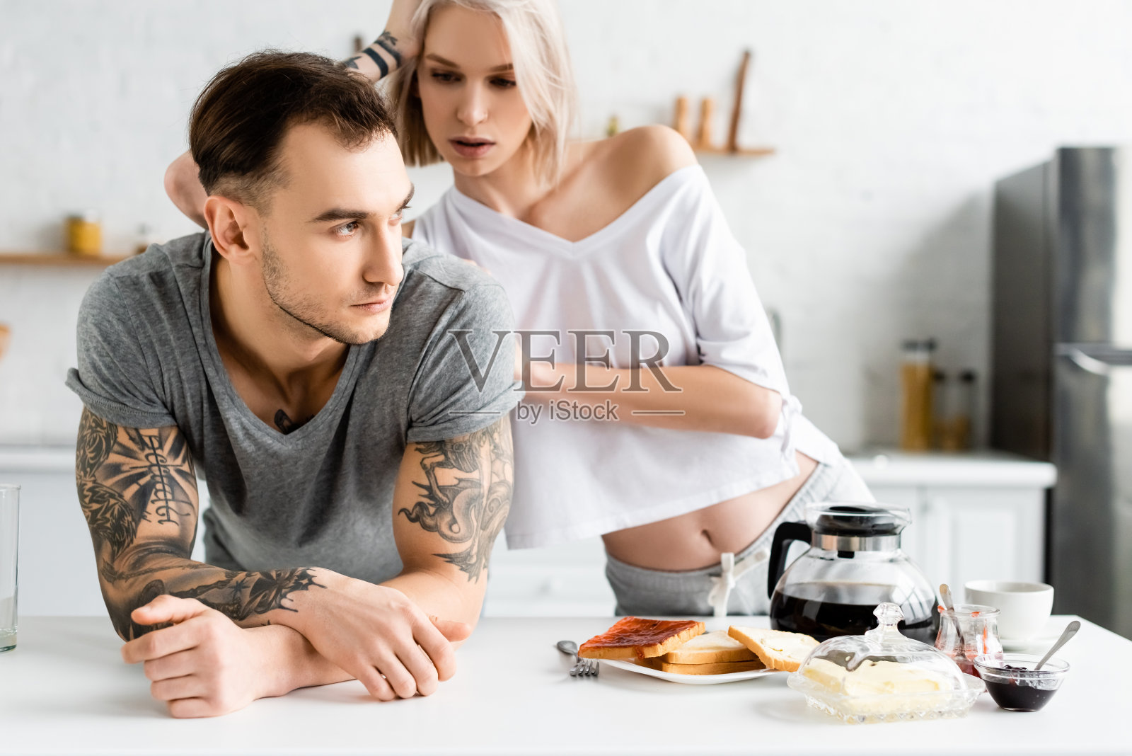 漂亮女人看着漂亮的纹身男友在餐桌上的早餐旁照片摄影图片