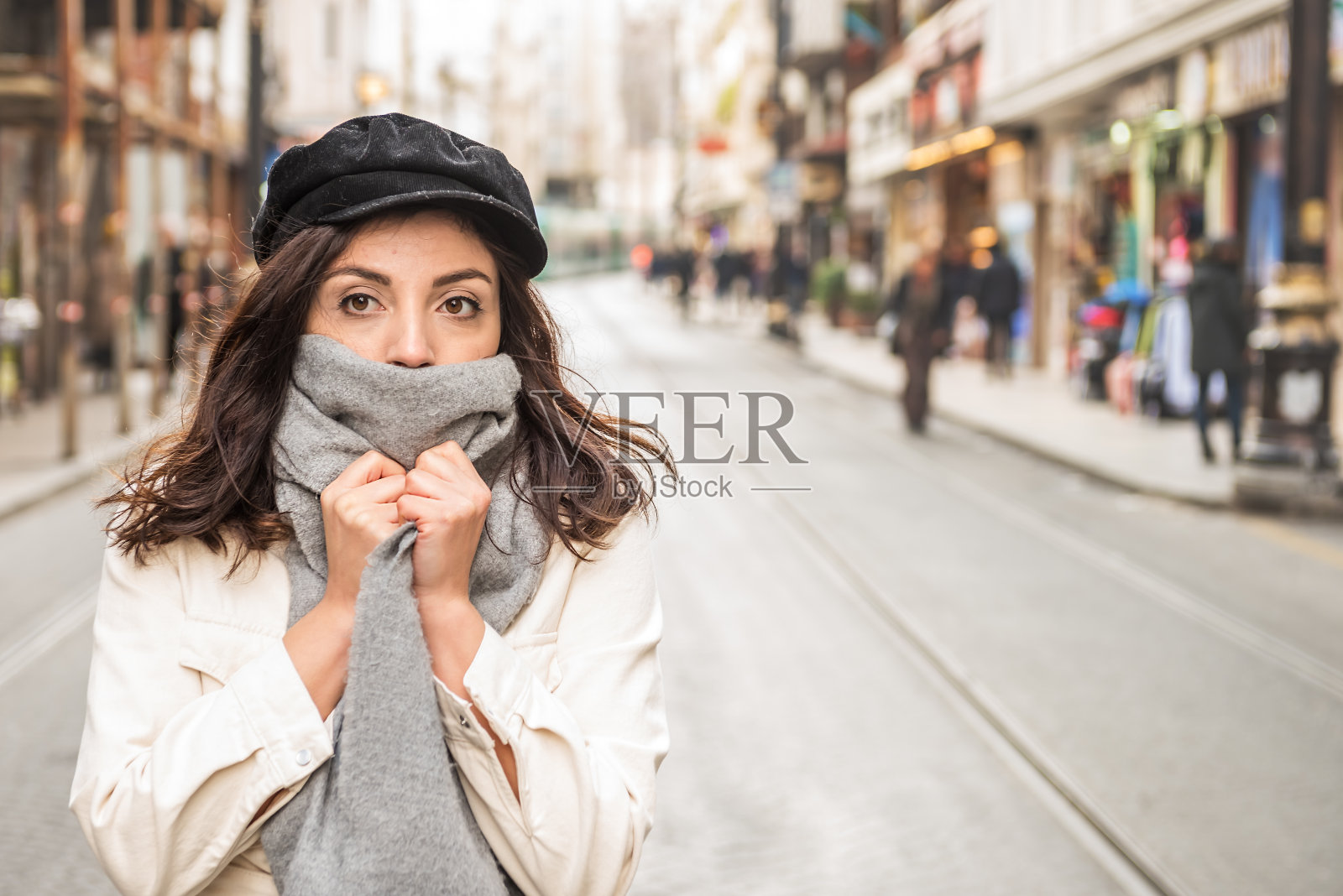 年轻漂亮的女人用羊毛围巾遮住脸。照片摄影图片