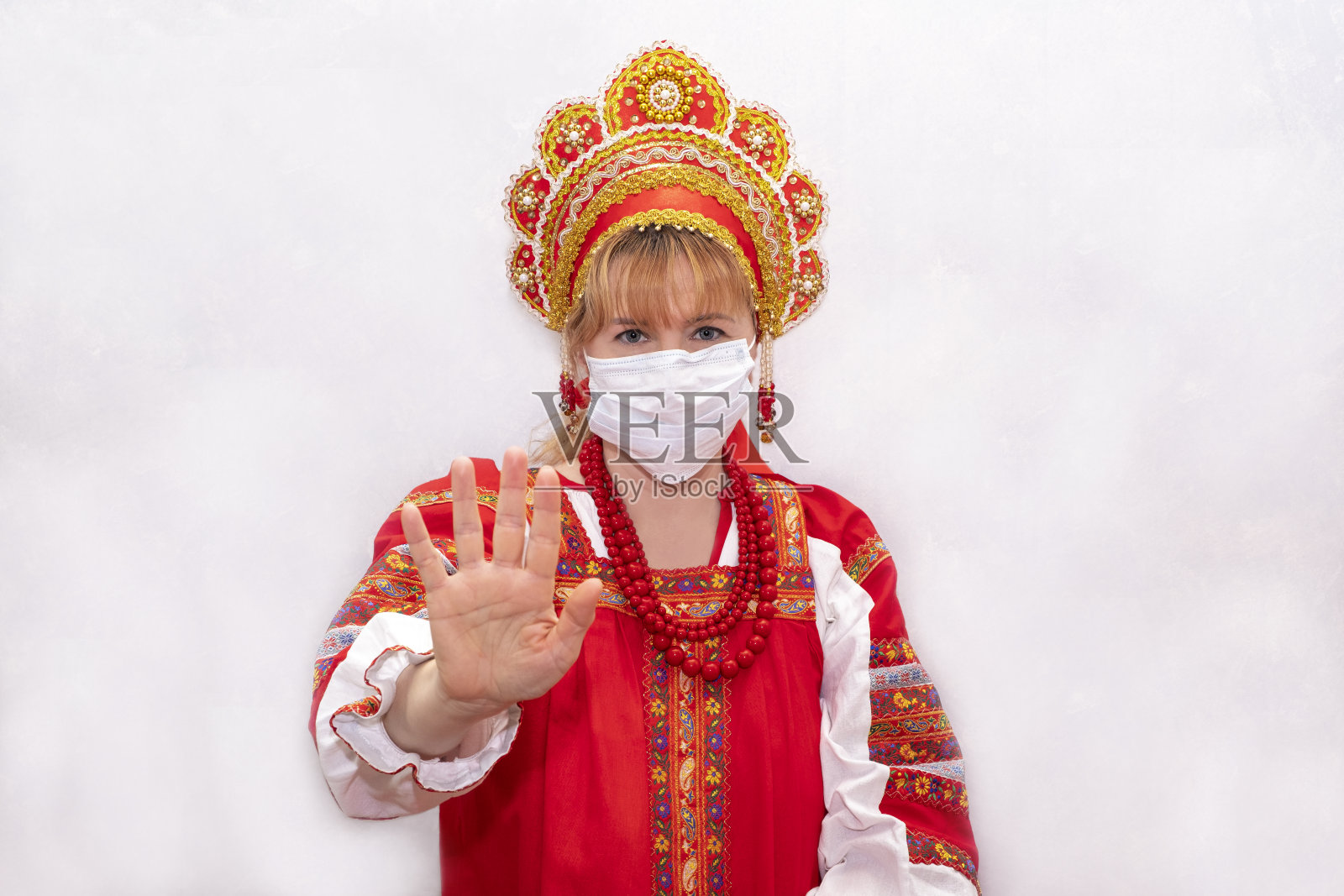穿着传统民族服装的女孩。戴着防护面具的女孩伸出手做了个停止的手势。阻止病毒。照片摄影图片