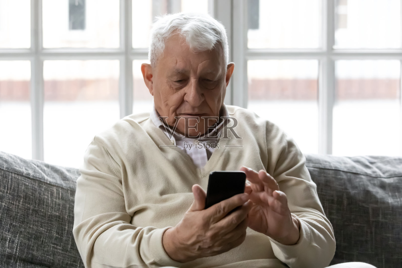 白发苍苍的80年代老人坐在沙发上玩智能手机照片摄影图片