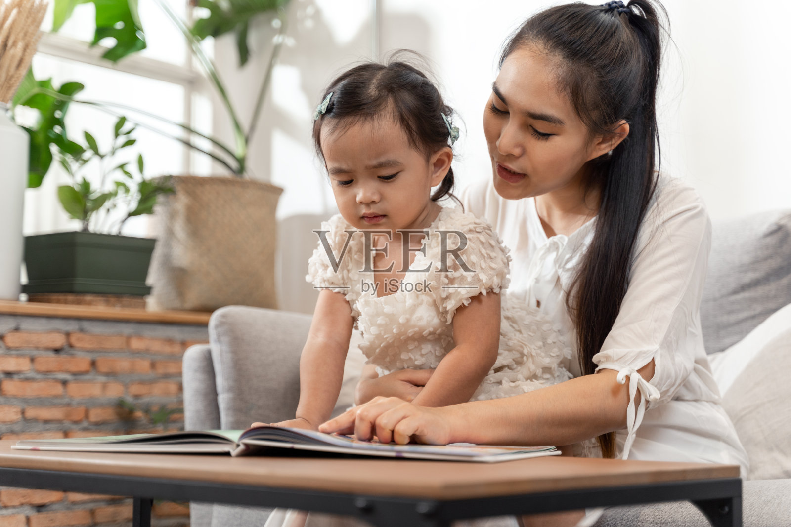 亚洲年轻美丽的母女坐在沙发上，幸福地读着一本书故事照片摄影图片