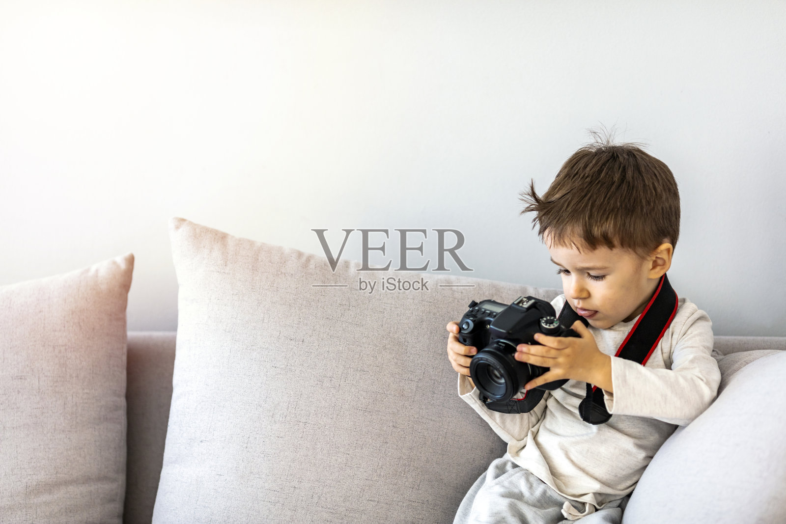 可爱可爱的小男孩坐在客厅的沙发上，玩着相机照片摄影图片