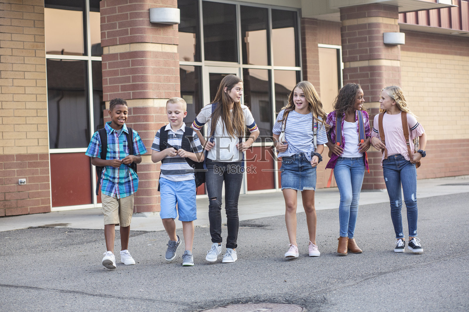 每天放学后离开学校的一大群形形色色的孩子。学校的朋友们一起散步，一起谈论着他们的青春期前的孩子们在学校大楼前微笑的照片照片摄影图片