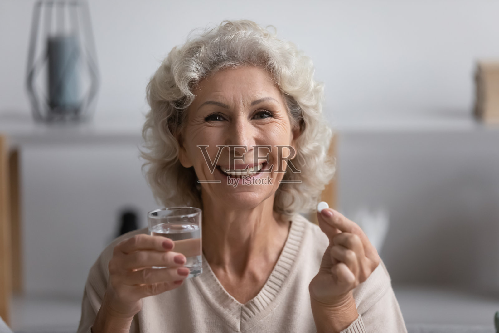 快乐的老年妇女拿着一杯水和药丸。照片摄影图片