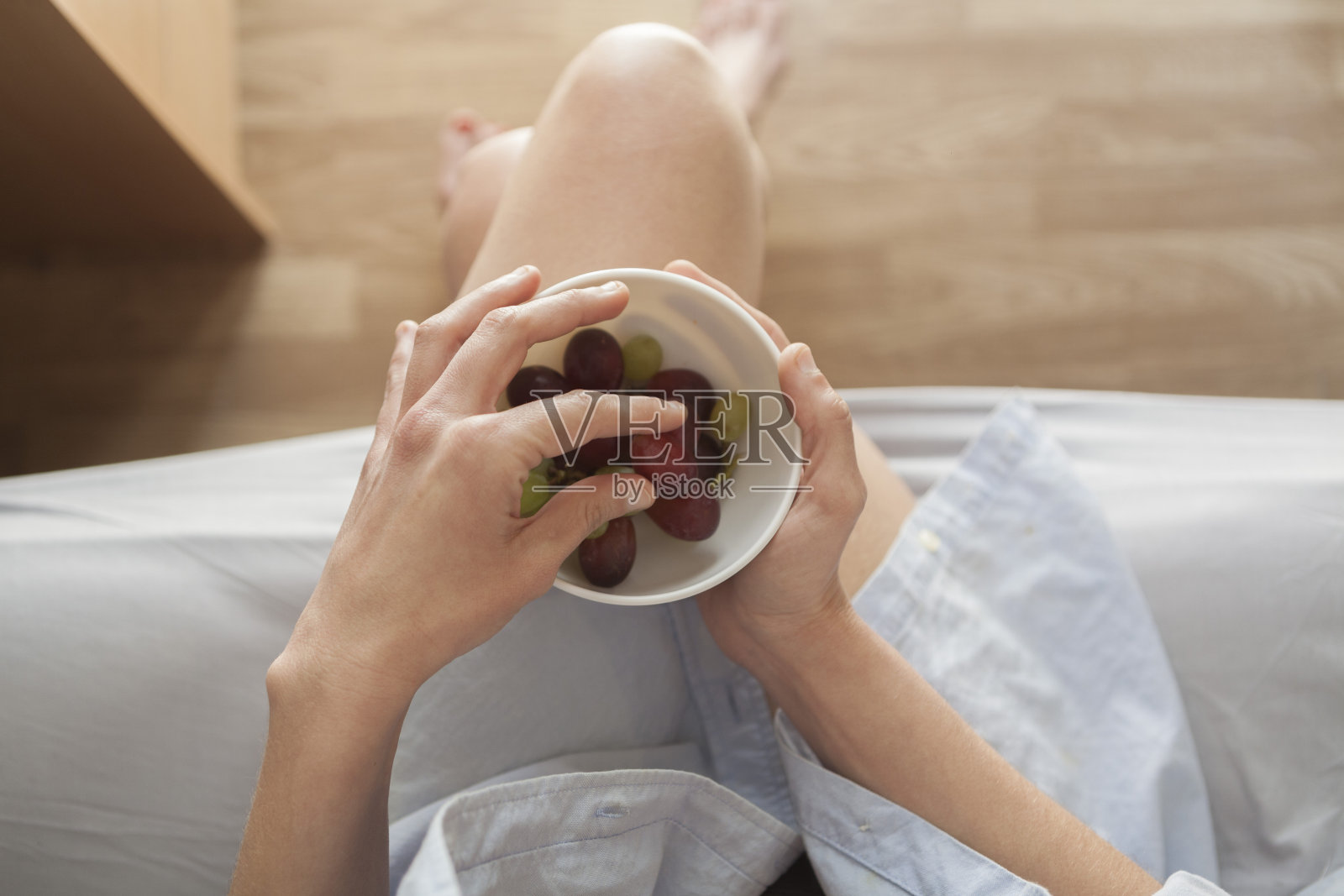 一个年轻的女人在她的房间里吃水果清晨坐在床上。一碗甜葡萄当早餐照片摄影图片
