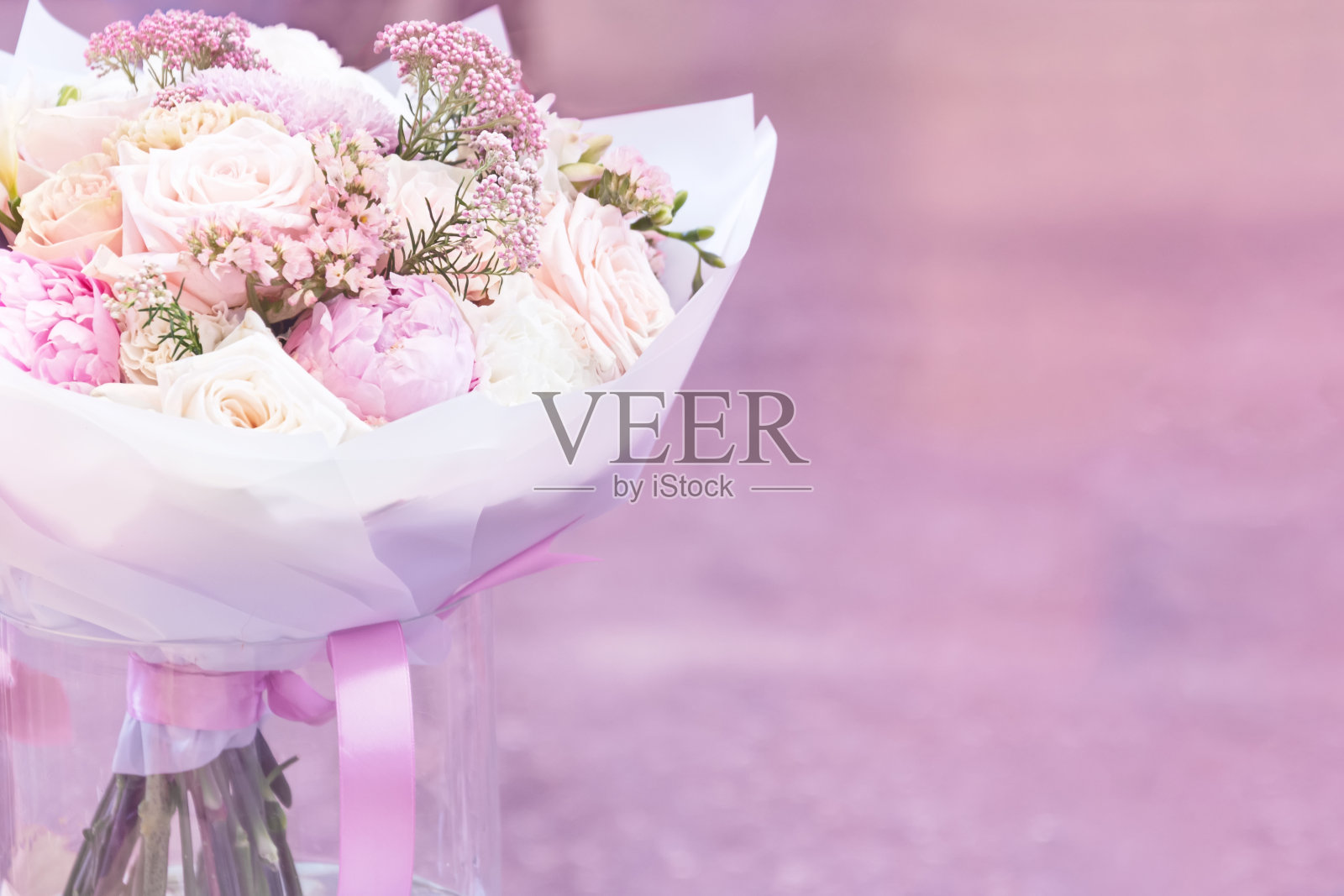 一束鲜花从粉红色的牡丹和玫瑰在白纸站在一个玻璃花瓶在粉红色的背景。概念背景、鲜花。照片摄影图片