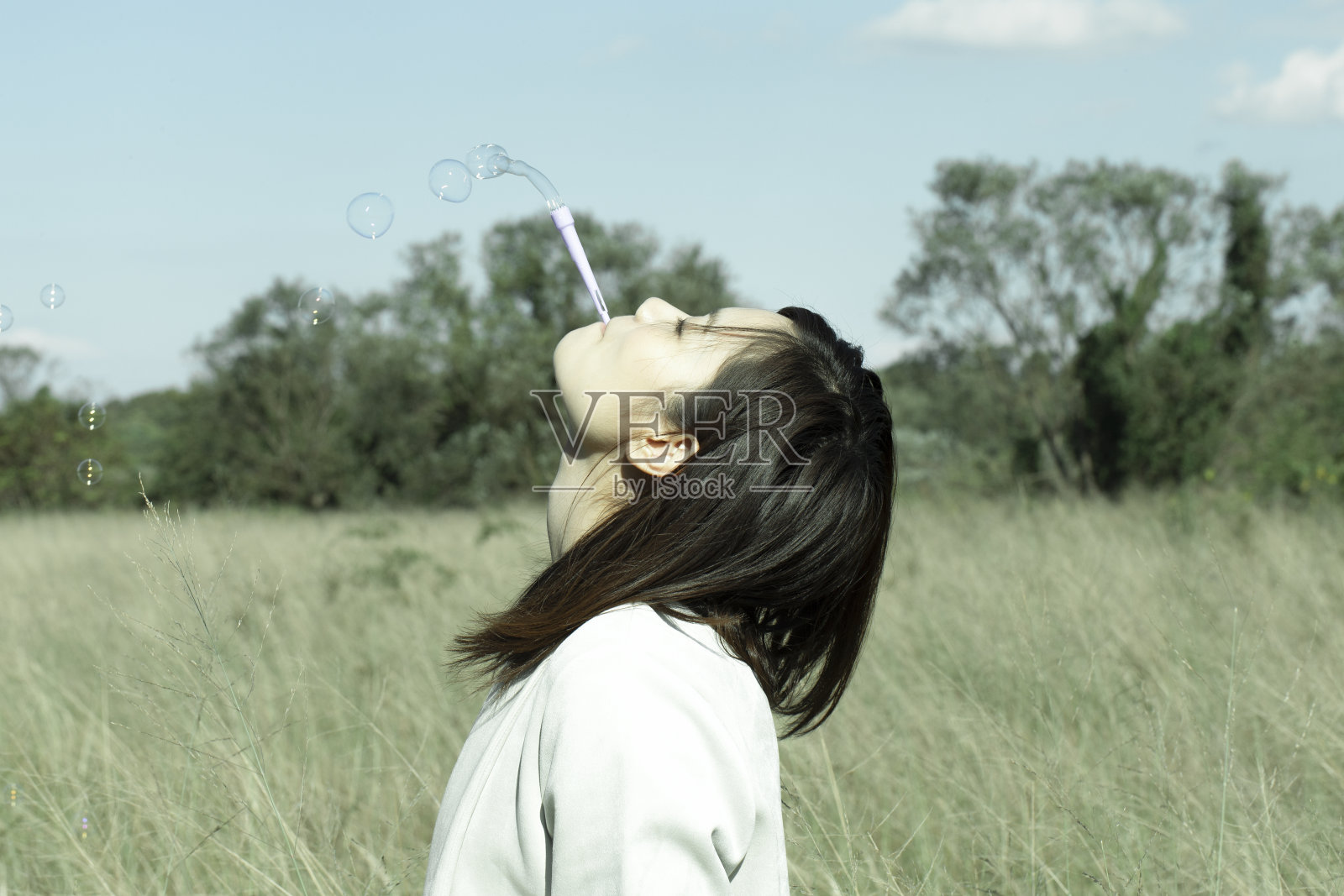 草原上，一个漂亮的年轻女子，正捧着肥皂泡望着天空。照片摄影图片