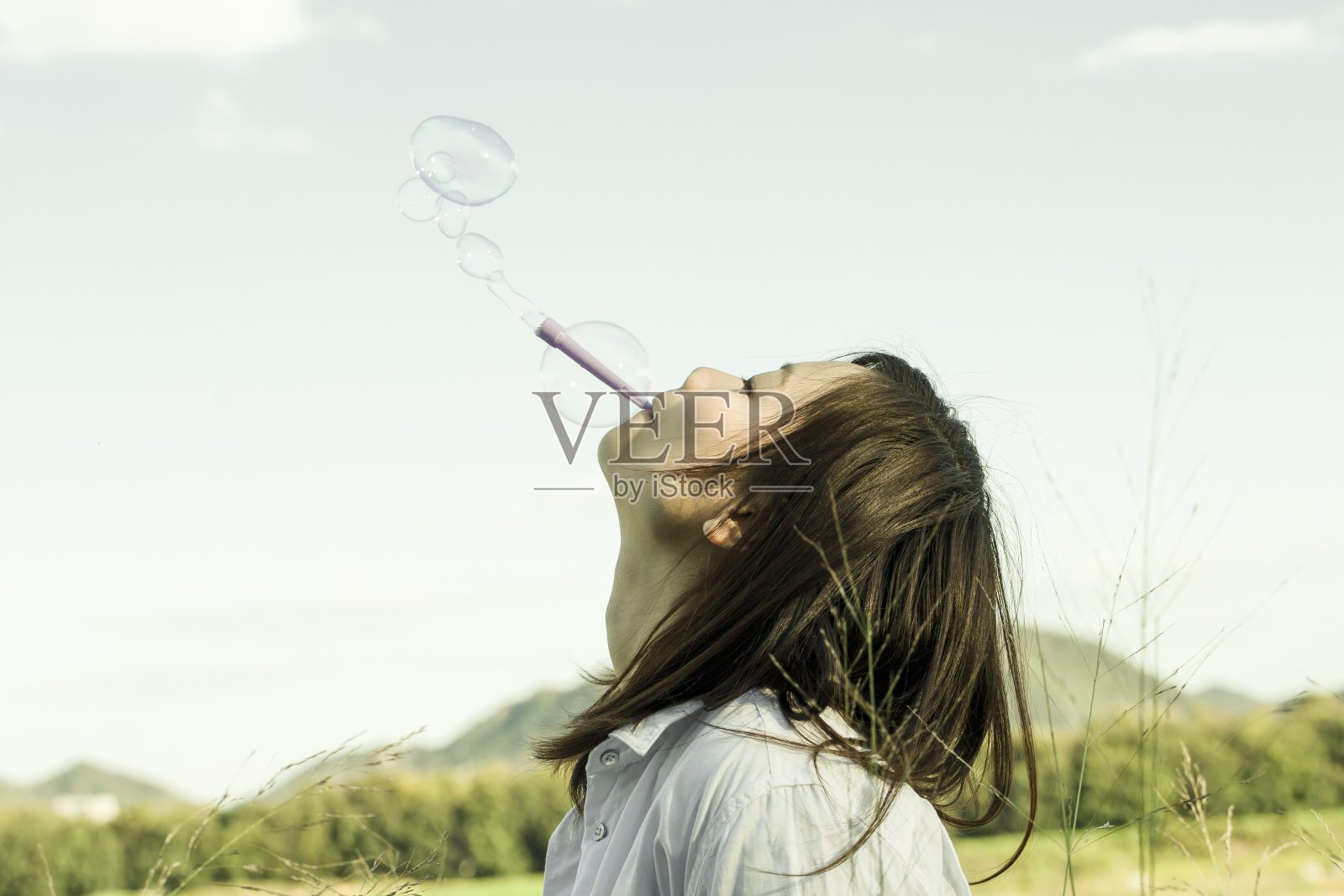 在一个阳光明媚的日子里，一个年轻女子在草地上玩肥皂泡。照片摄影图片