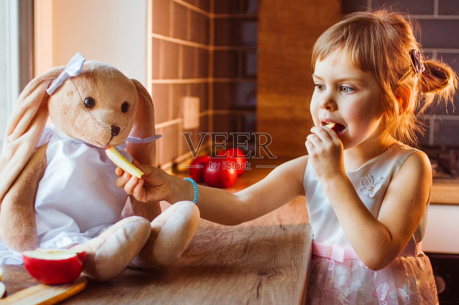 小女孩玩着兔子软软的玩具，喂它新鲜的苹果片照片摄影图片