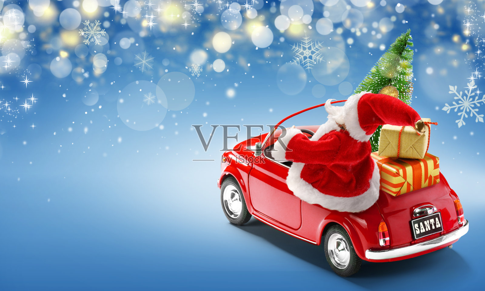 圣诞老人开着带礼盒的红色汽车，蓝色背景的圣诞树上挂着散景灯照片摄影图片