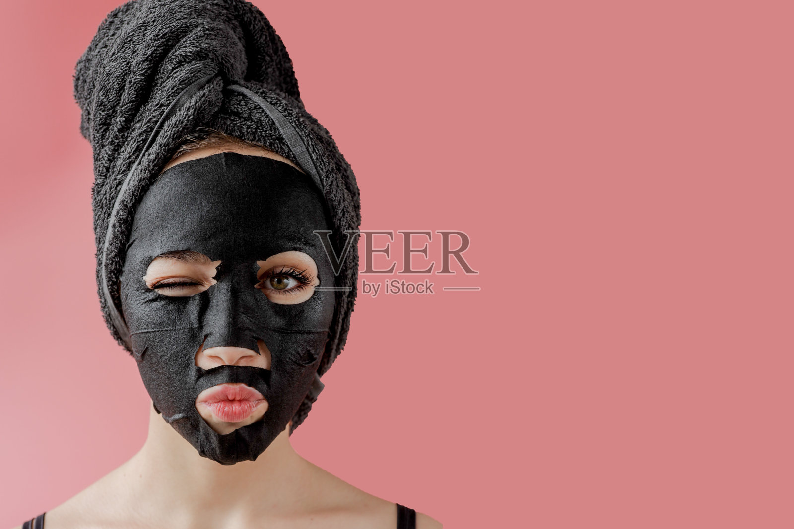 年轻女子将黑色化妆布面膜涂在粉色背景上。面部脱皮用炭面膜、spa美容、护肤、美容。近距离照片摄影图片
