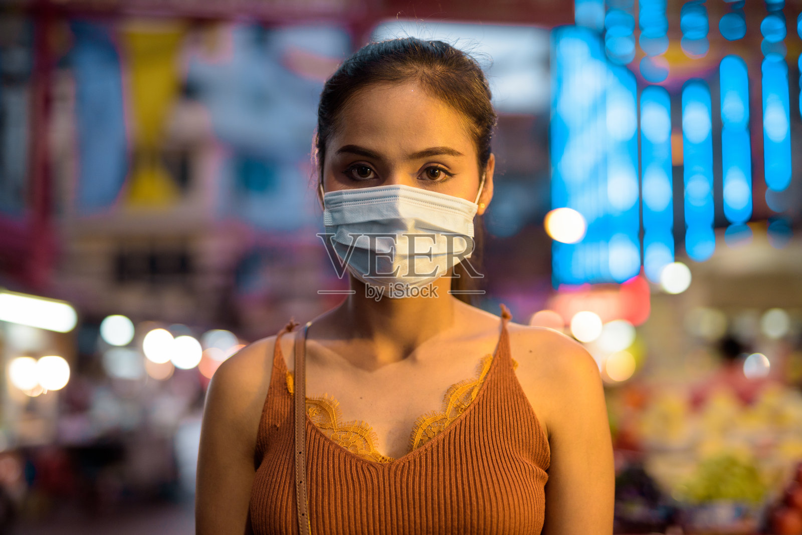 年轻的亚洲女游客戴着面罩，以防止华埠晚上爆发冠状病毒照片摄影图片