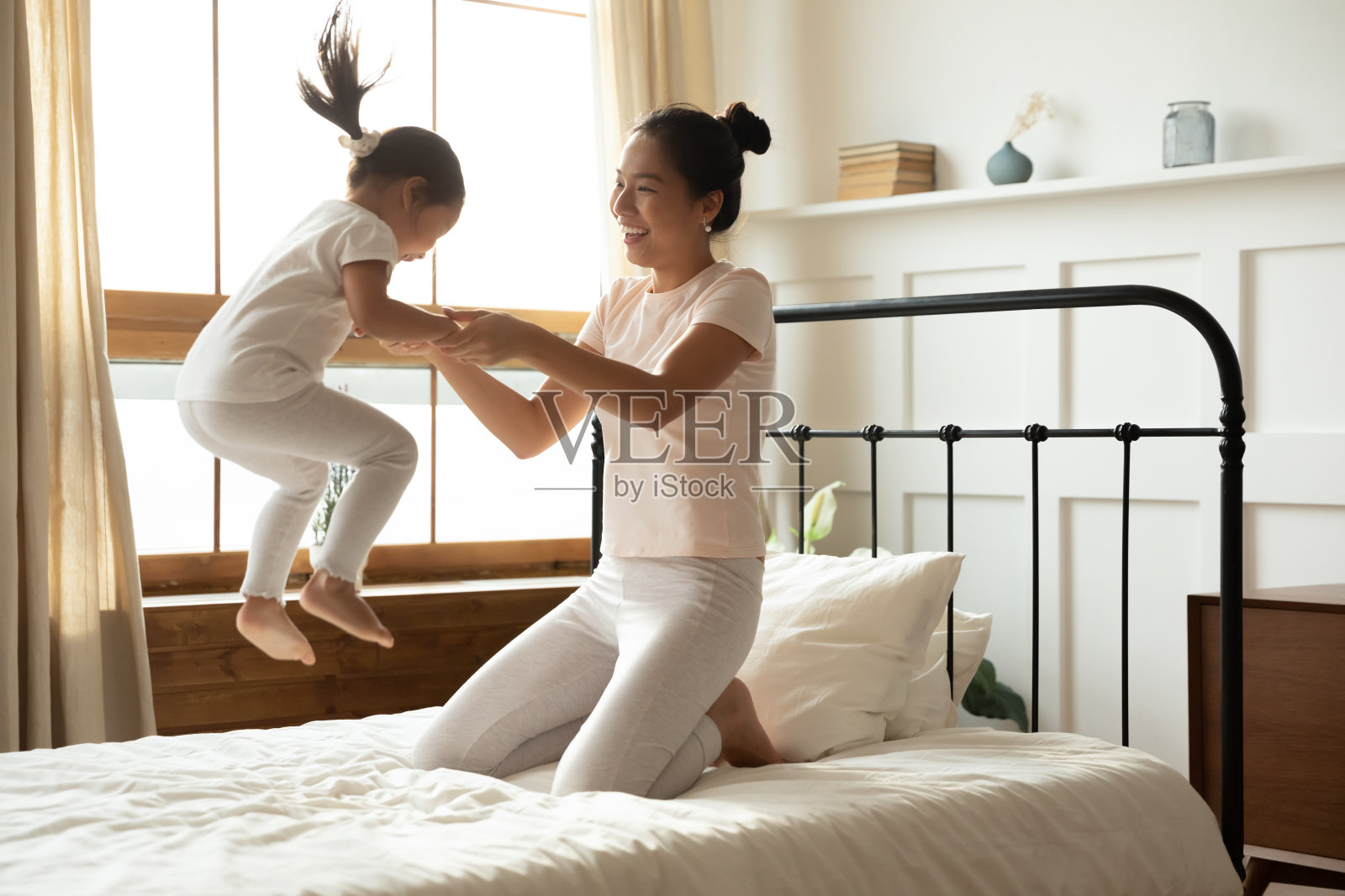 妈妈牵着小女儿在床上蹦蹦跳跳照片摄影图片