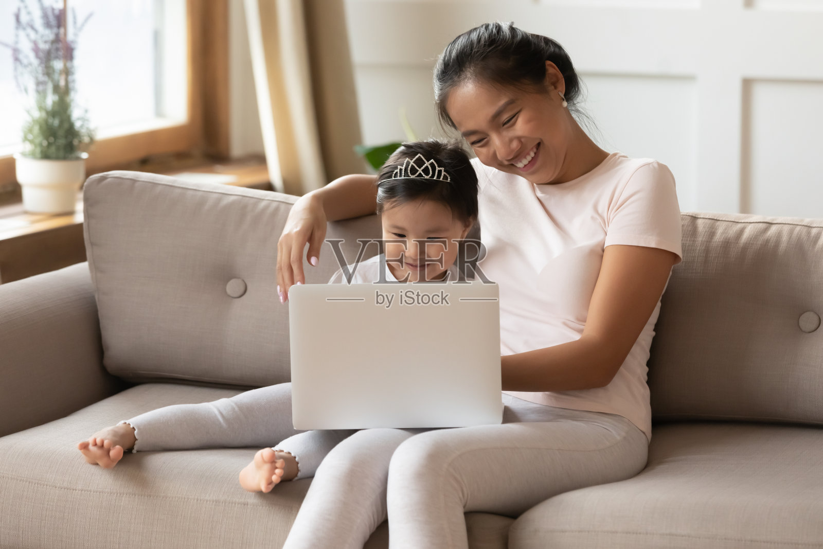 亚洲母亲女儿坐在沙发上看卡通片上的笔记本电脑照片摄影图片