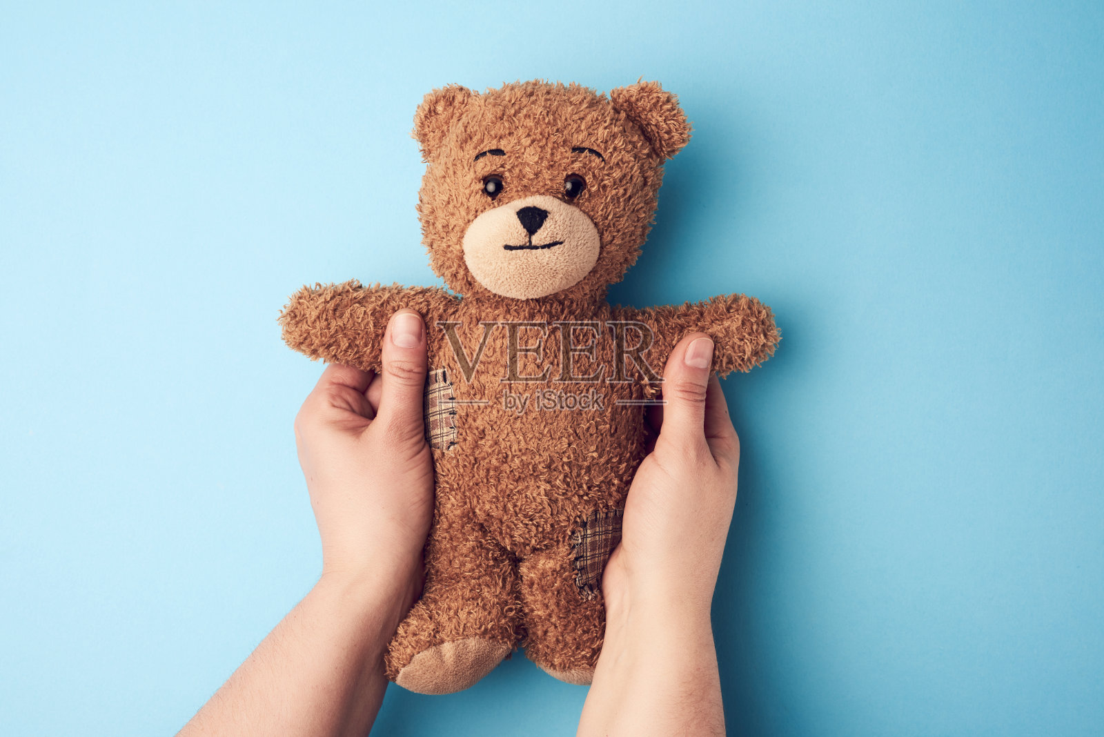 两个女人的手拿着一个小的棕色玩具熊在一个蓝色的bac照片摄影图片