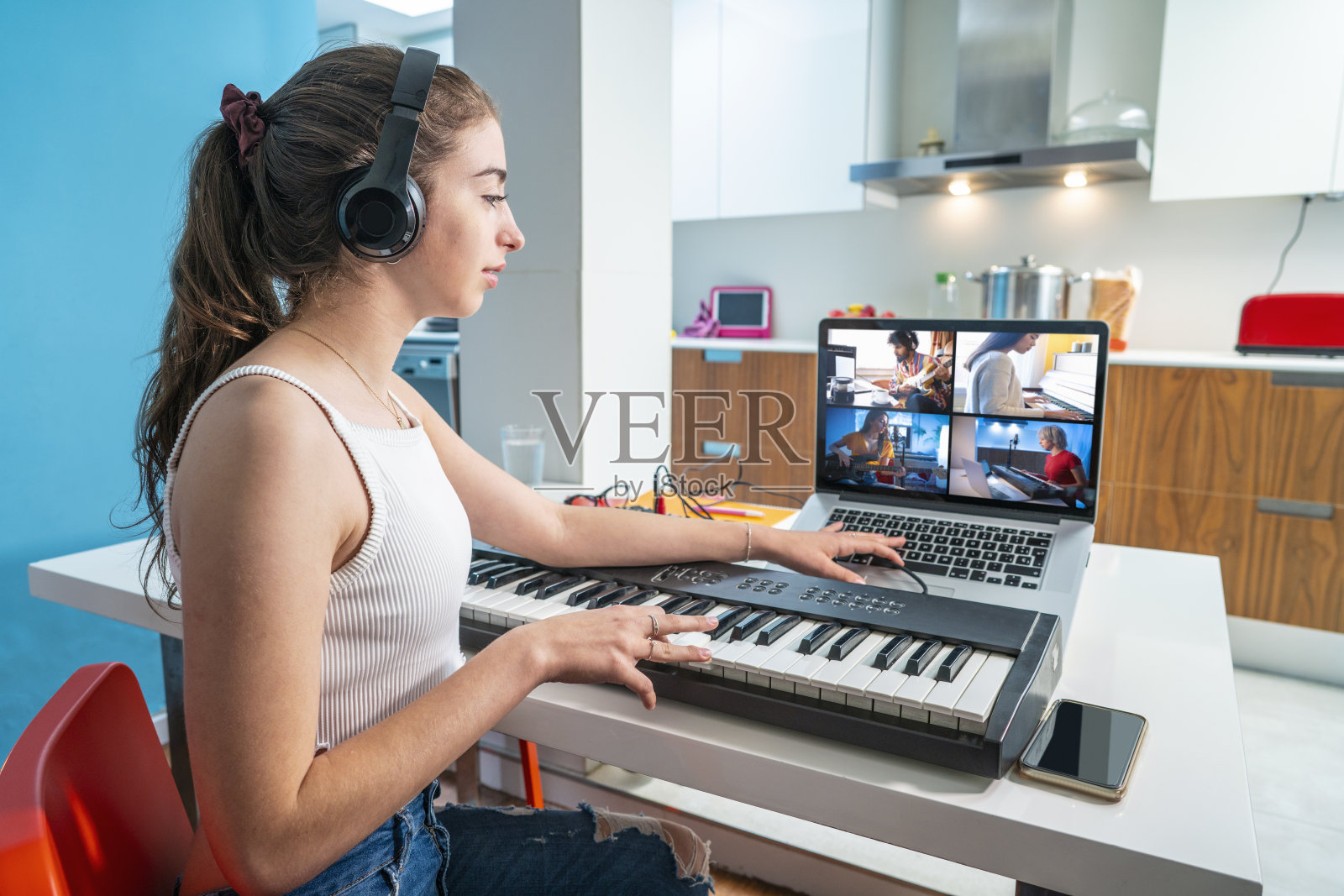 与音乐电话会议十几岁的女孩在家里厨房和她的乐队玩键盘照片摄影图片