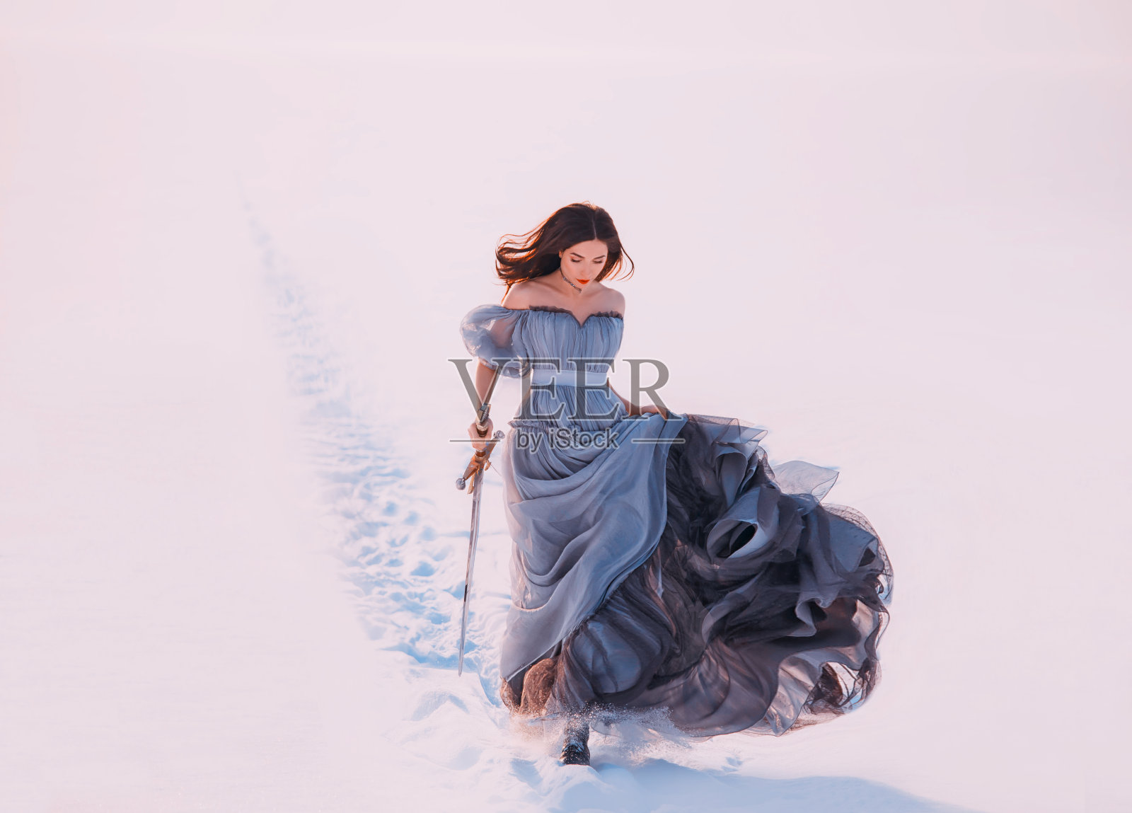 幻想孤独公主红发精灵走冬霜白雪的自然。年轻美女跑步。女王手持魔法剑。蓝色丝质长裙飘飘荡荡，随风飘动照片摄影图片