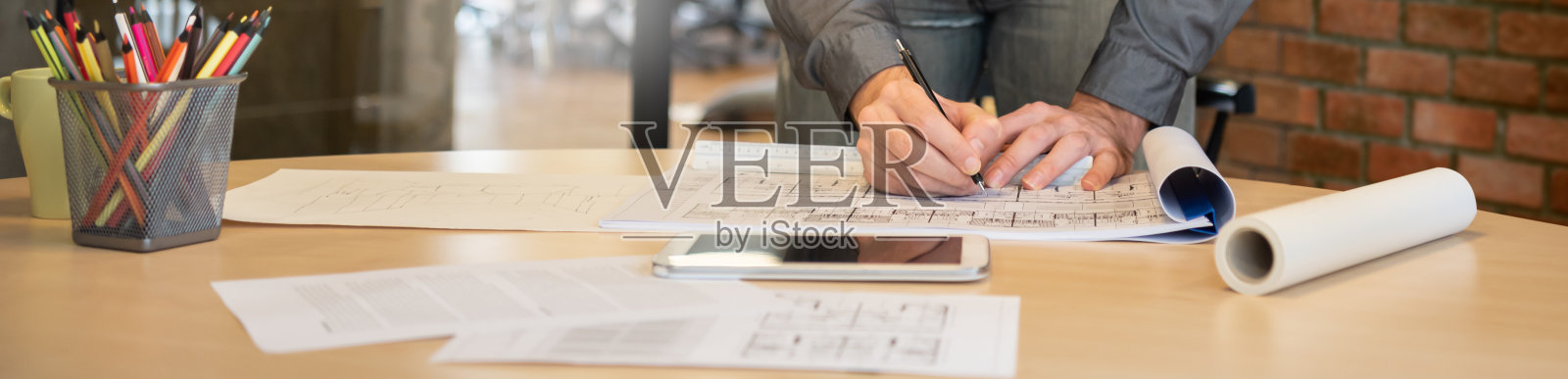 专业室内男性设计师在工作空间的木桌上绘制蓝图。建筑师在办公室里手绘设计建筑项目的文书工作。照片摄影图片