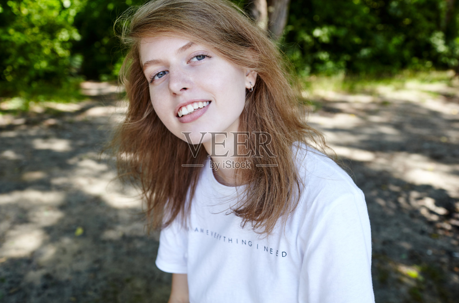 美丽迷人的女人在白色t恤摆姿势在夏季公园。活泼微笑的女孩在户外休息照片摄影图片
